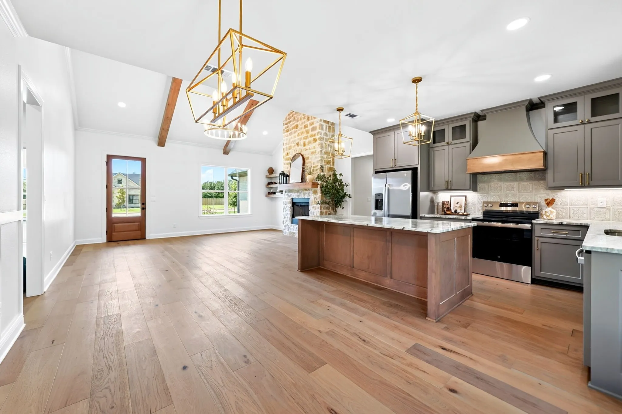 Open-concept living area with wood-finish flooring, exposed ceiling beams, and a stone fireplace
