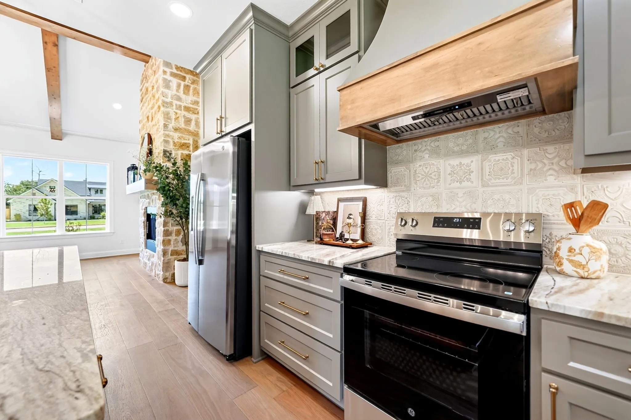 Stainless steel appliances, light wood-finish flooring, stone-clad fireplace, vaulted ceiling with exposed beam, and patterned backsplash