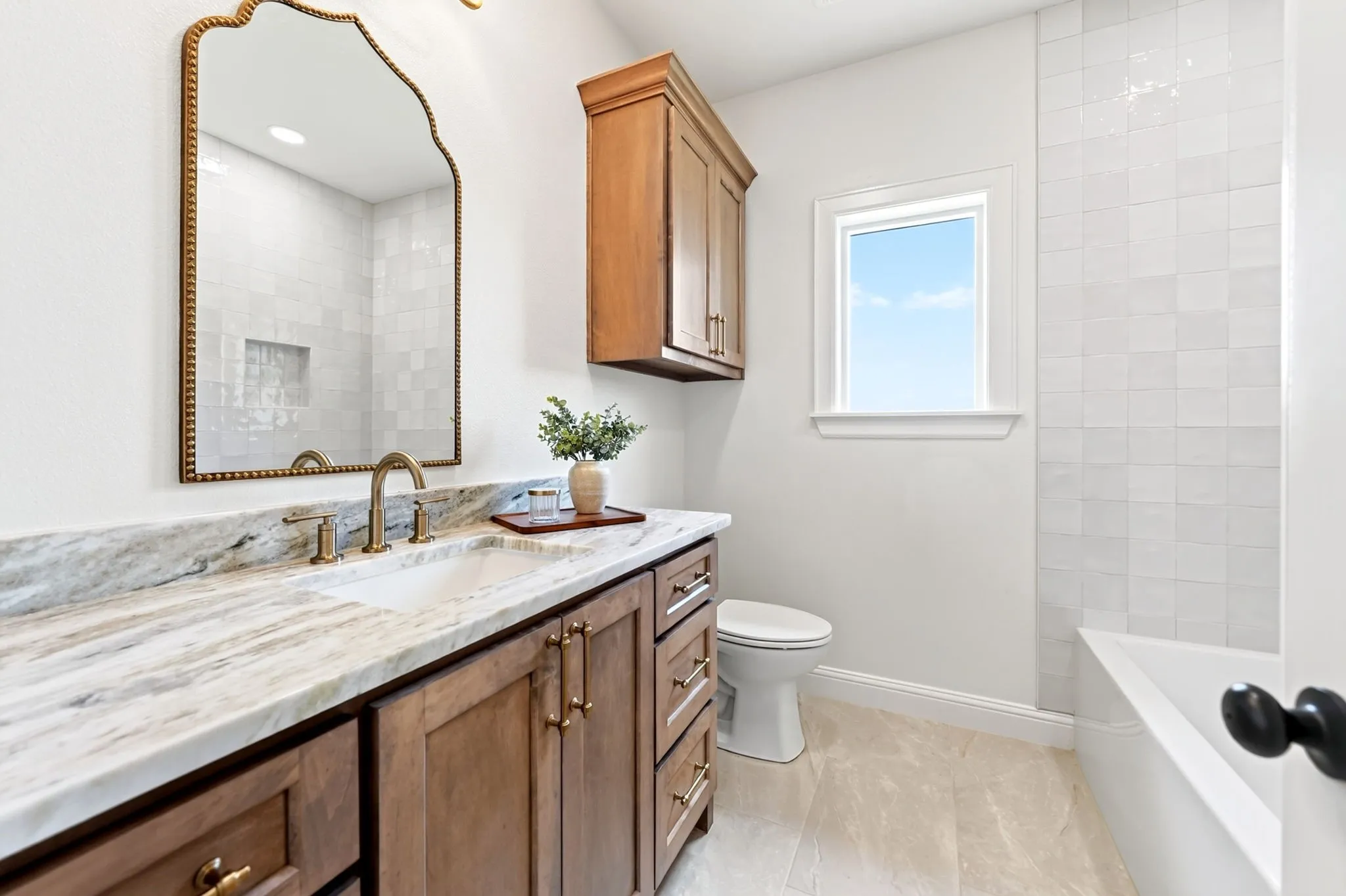 Built-in vanity with wood cabinetry, light-toned stone countertop, brass-finish faucet, and an ornate mirror
