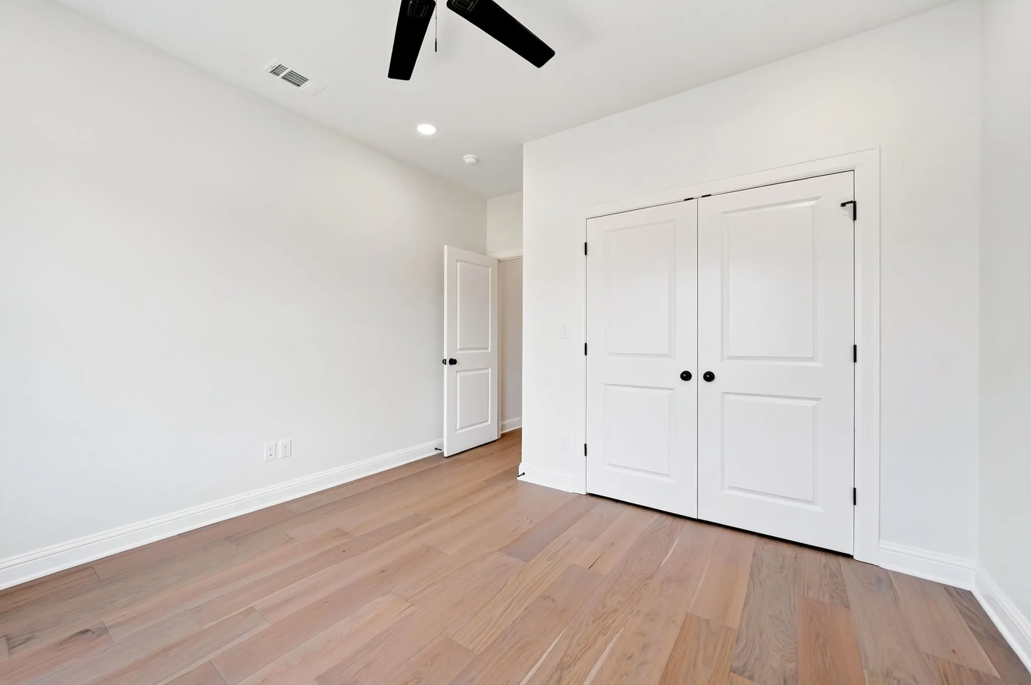 Wood-finish flooring, white walls, white paneled doors, matte black door hardware, and a ceiling-mounted fan