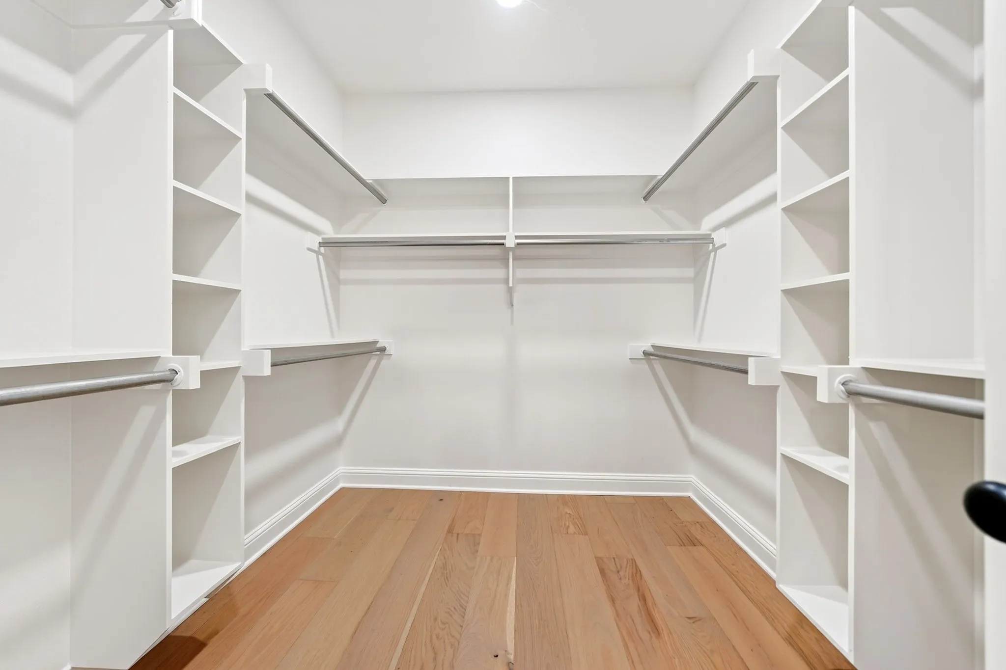 Custom closet system featuring built-in shelving, multiple hanging rods, and wood-finish flooring