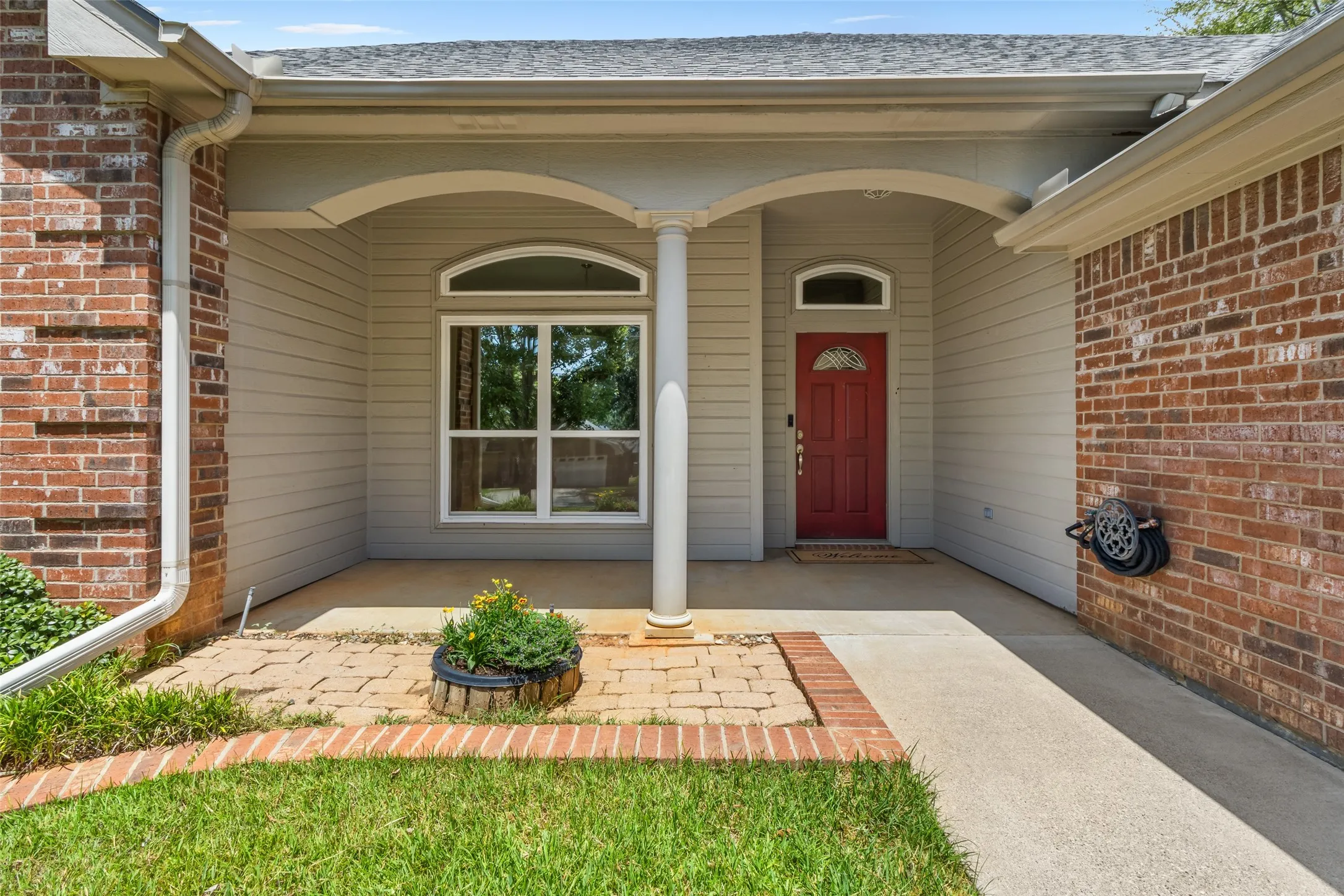 Brick exterior facade with a covered entry, decorative arched window, and a red paneled entry door with an arched transom