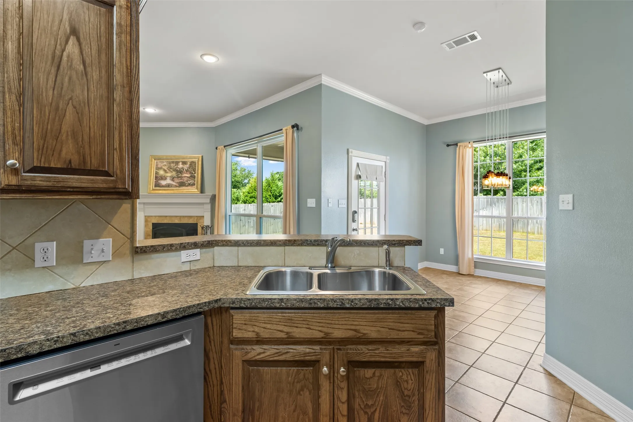 Kitchen featuring wood-finish cabinetry, a double basin stainless steel sink, and speckled countertops