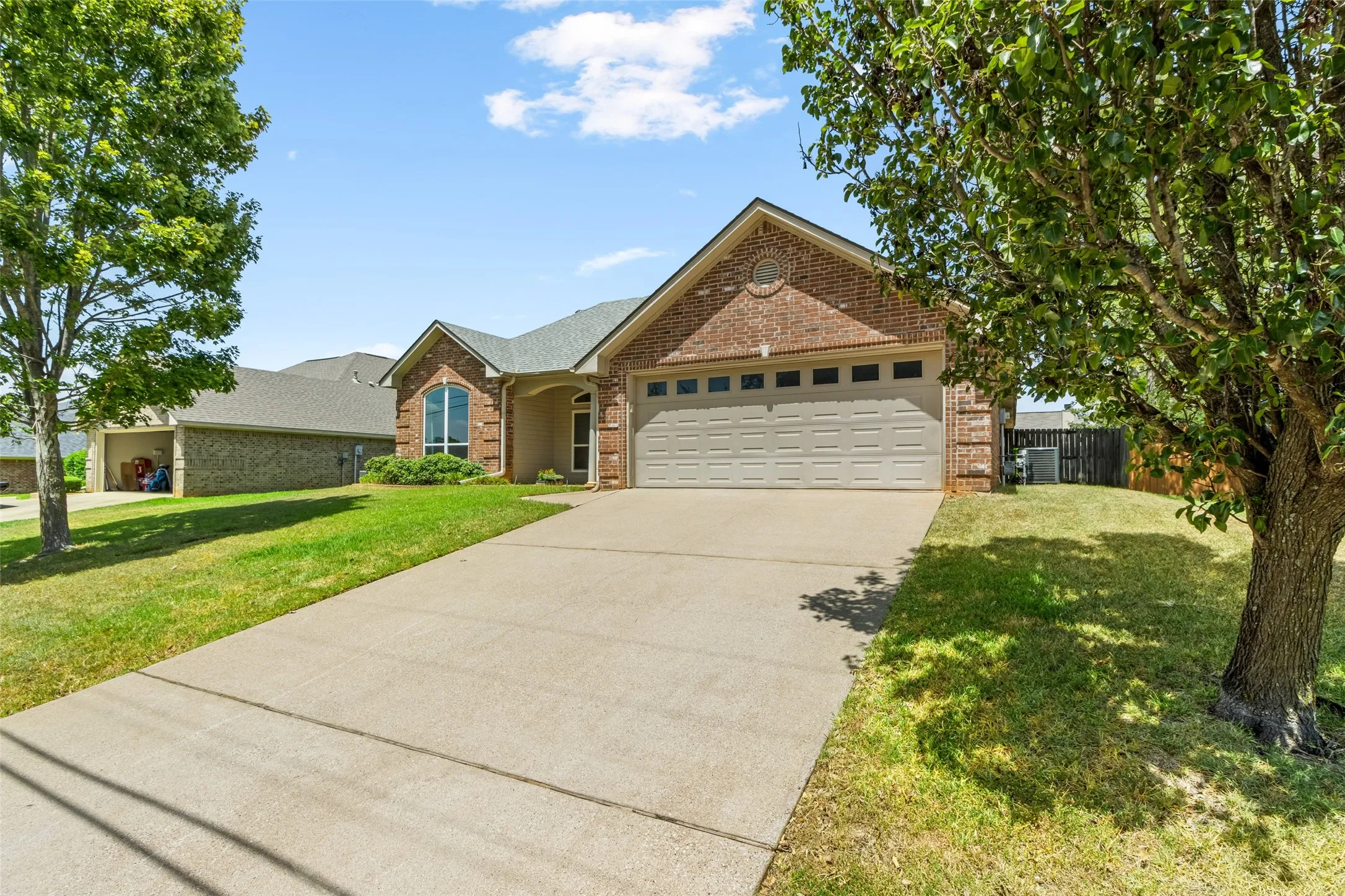 Brick exterior with a two-car garage, concrete driveway, and mature landscaping