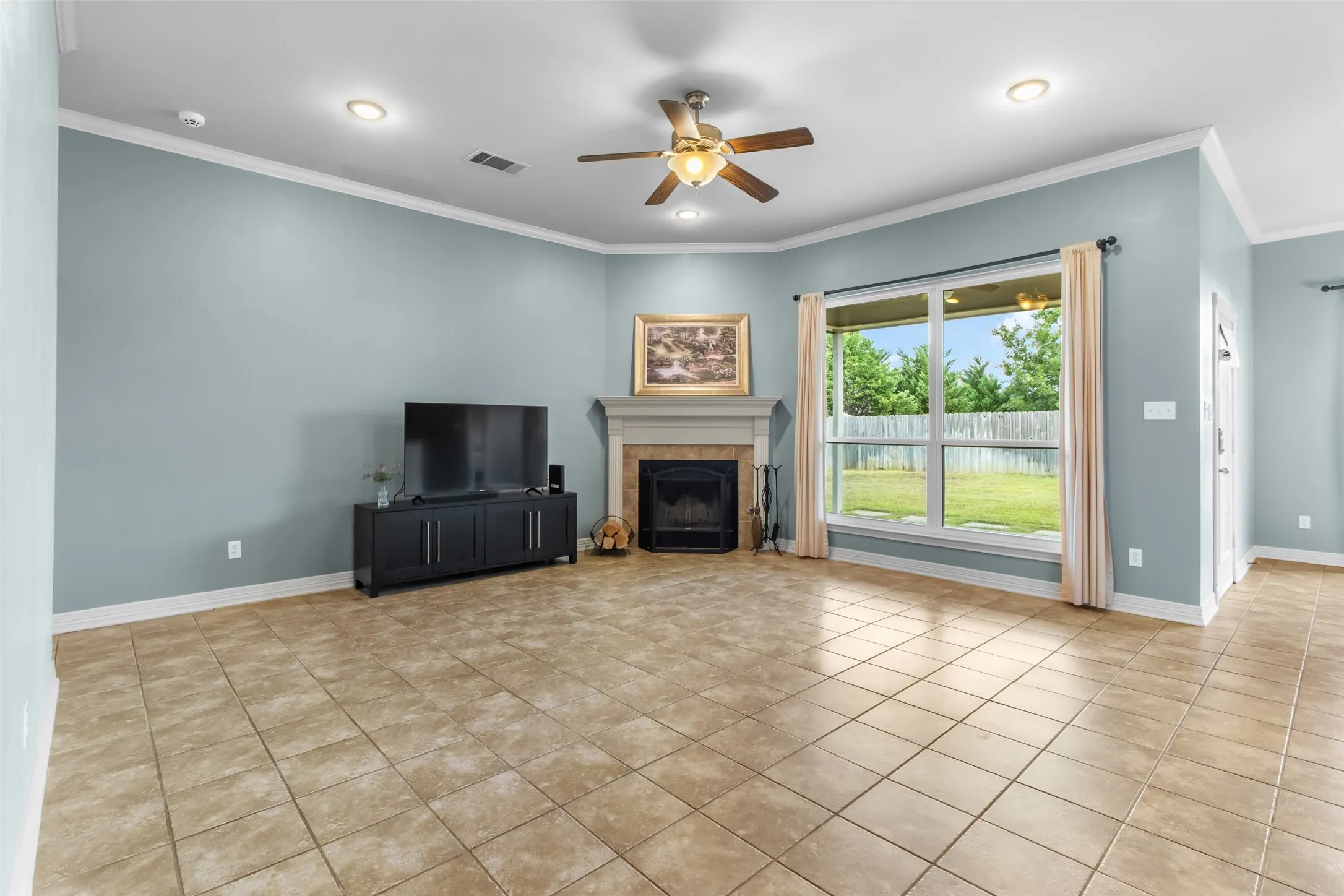 Tiled flooring, corner fireplace with mantel, ceiling fan with integrated lighting, recessed lighting, and a large window overlooking the backyard