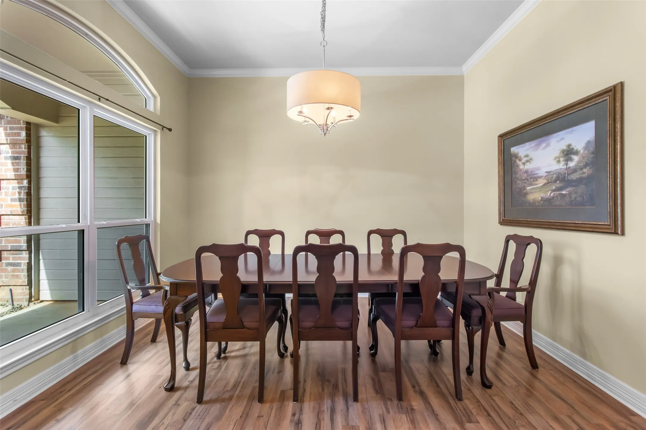 Wood-finish flooring, crown molding, and a large arched window