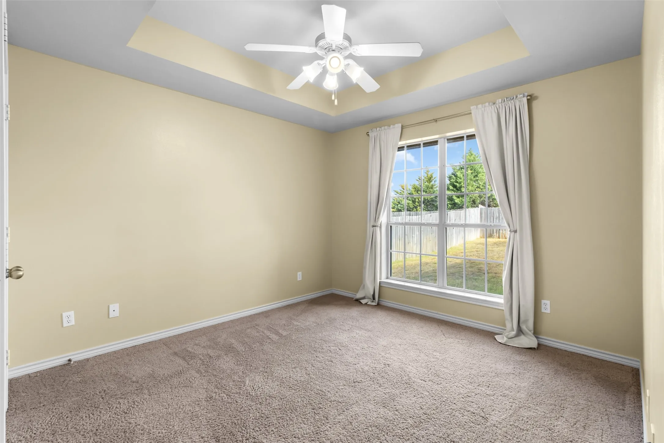 Tray ceiling with a ceiling fan, carpet flooring, and a large window