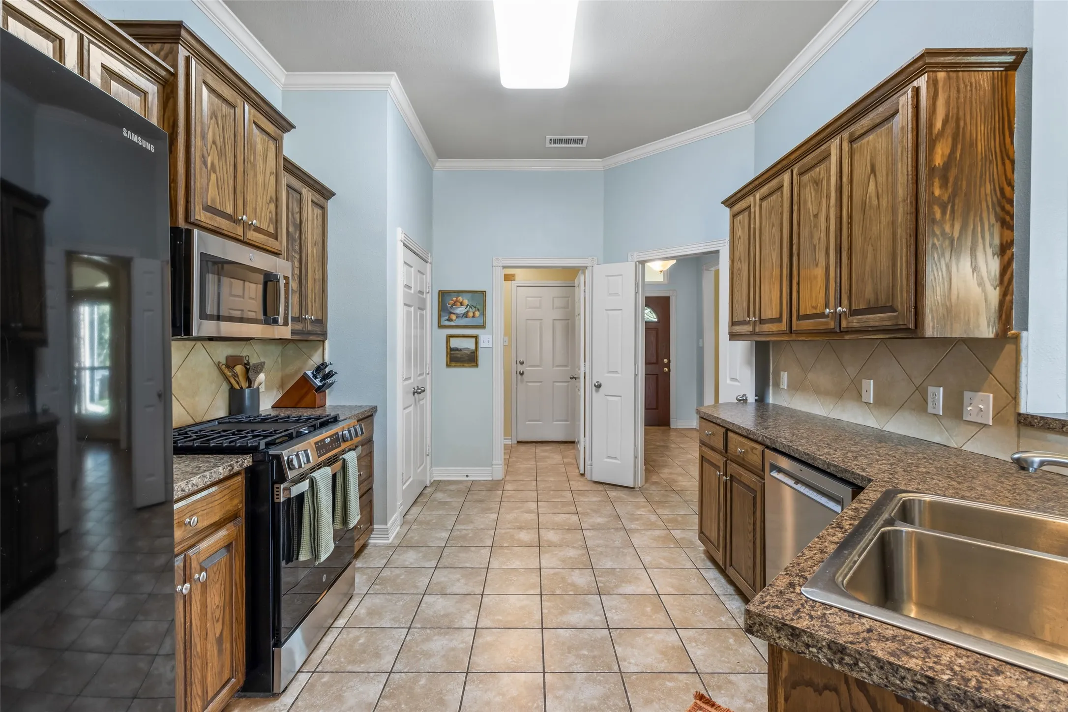 Tile flooring, wood-finish cabinetry, stainless steel appliances, granite-style countertops, and a tile backsplash