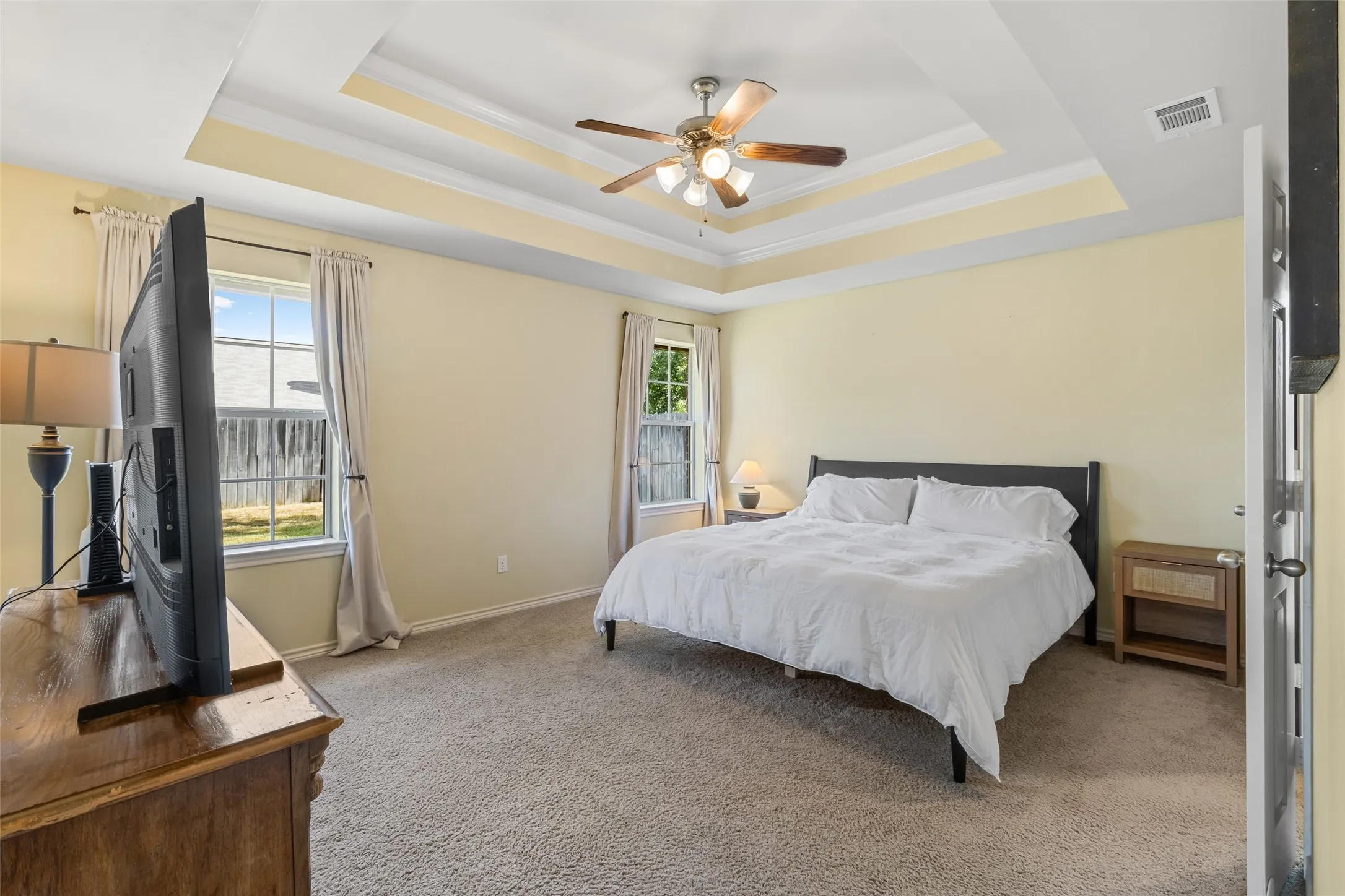 Tray ceiling with crown molding, ceiling fan, two windows, wall-to-wall carpeting, and light-colored walls