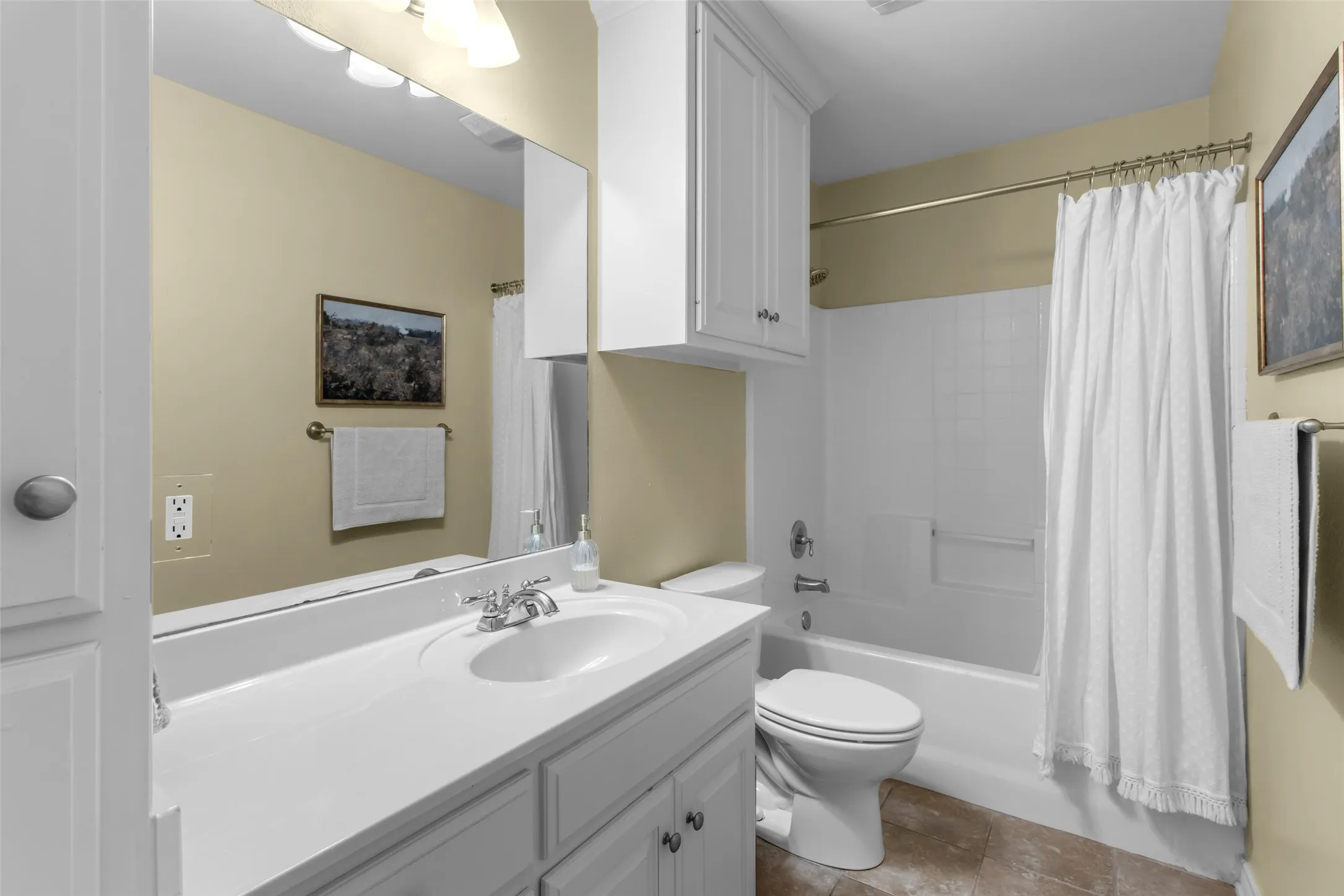 White vanity with an integrated sink and chrome faucet, large vanity mirror, white built-in cabinetry, and a white bathtub with a shower