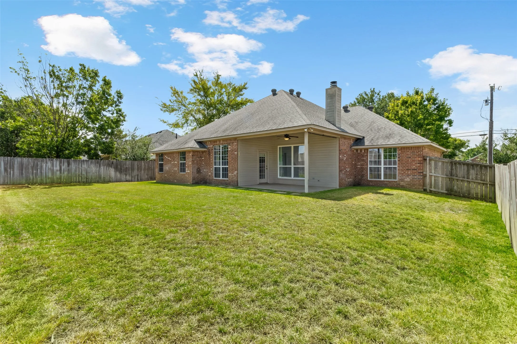 Expansive green yard with perimeter fencing and a covered patio featuring an outdoor ceiling fan