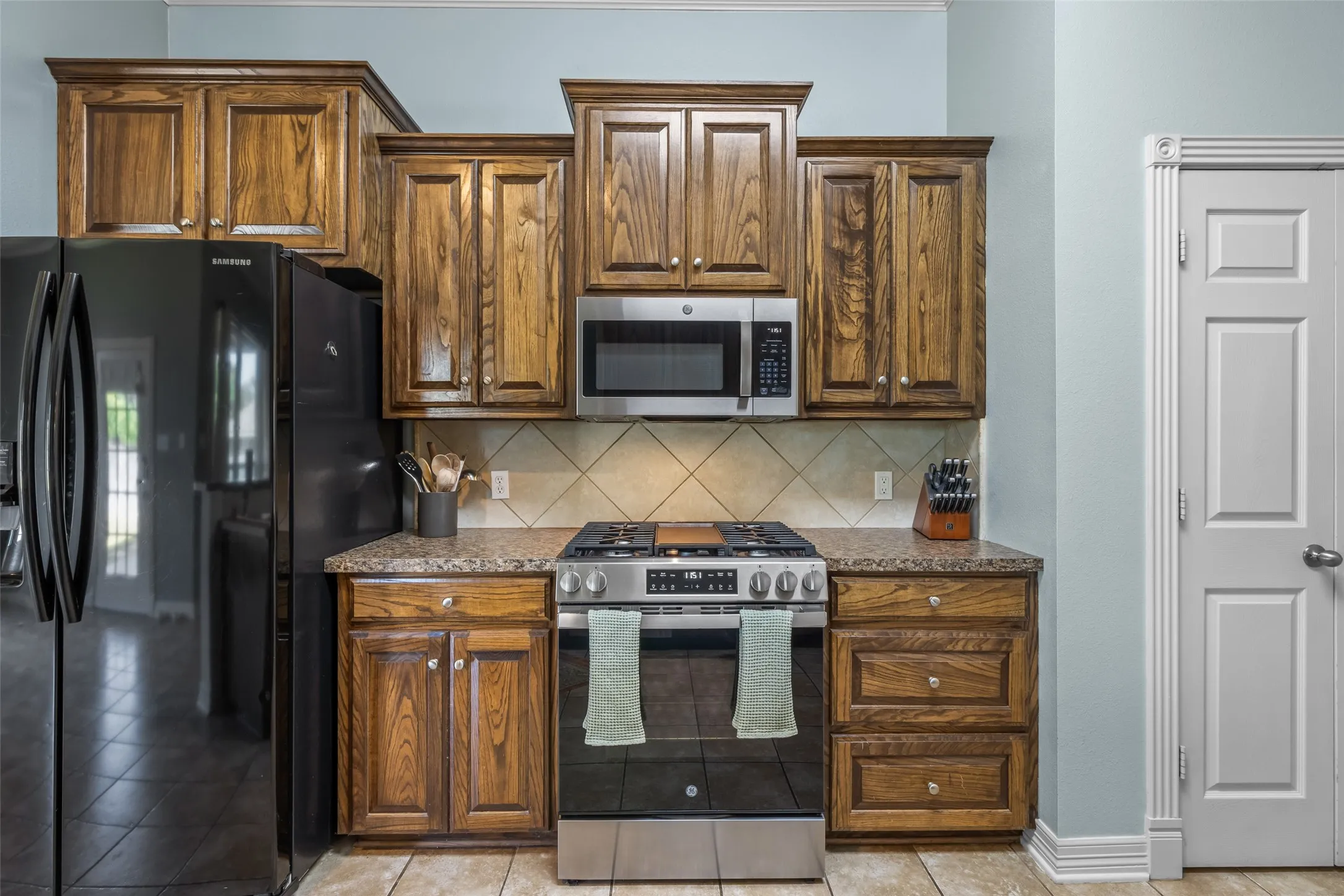 Kitchen featuring wood cabinetry, stainless steel range, microwave, and a tile backsplash
