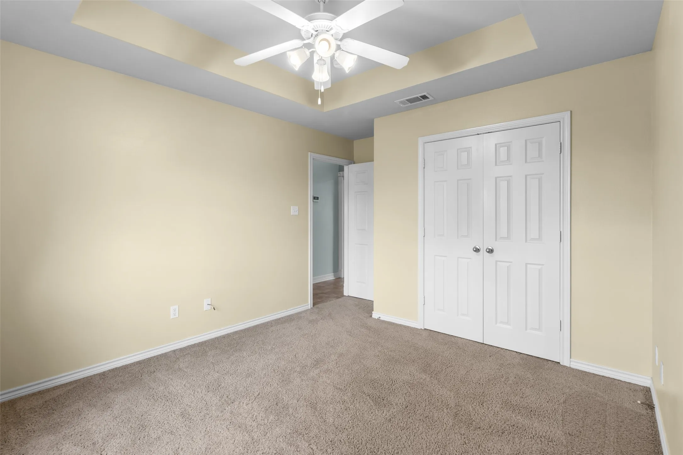 Tray ceiling with a ceiling fan, neutral wall paint, white trim, carpeted flooring, and paneled bifold doors