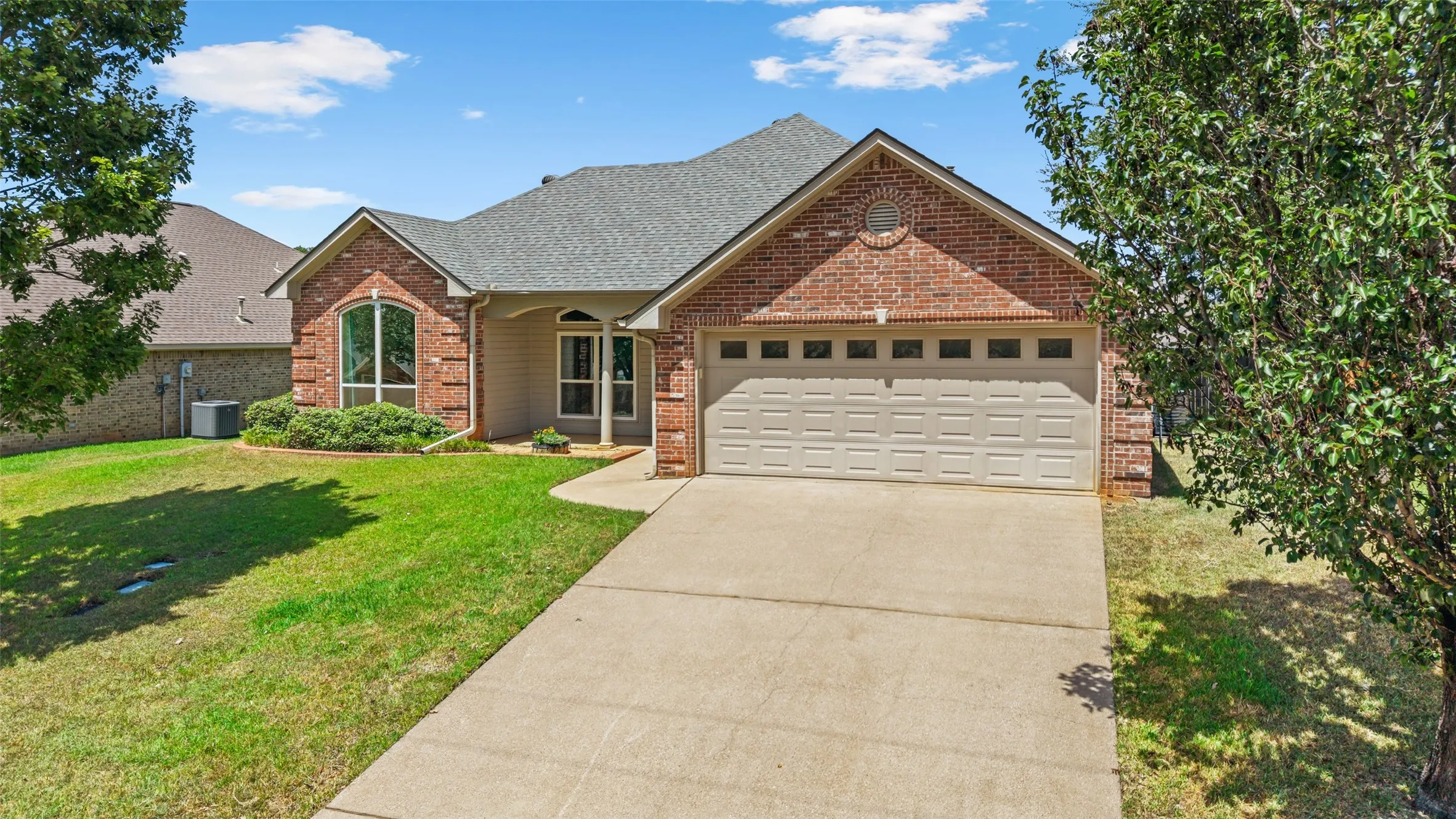Brick and siding exterior with an arched window, a two-car garage, a concrete driveway, and a shingle roof