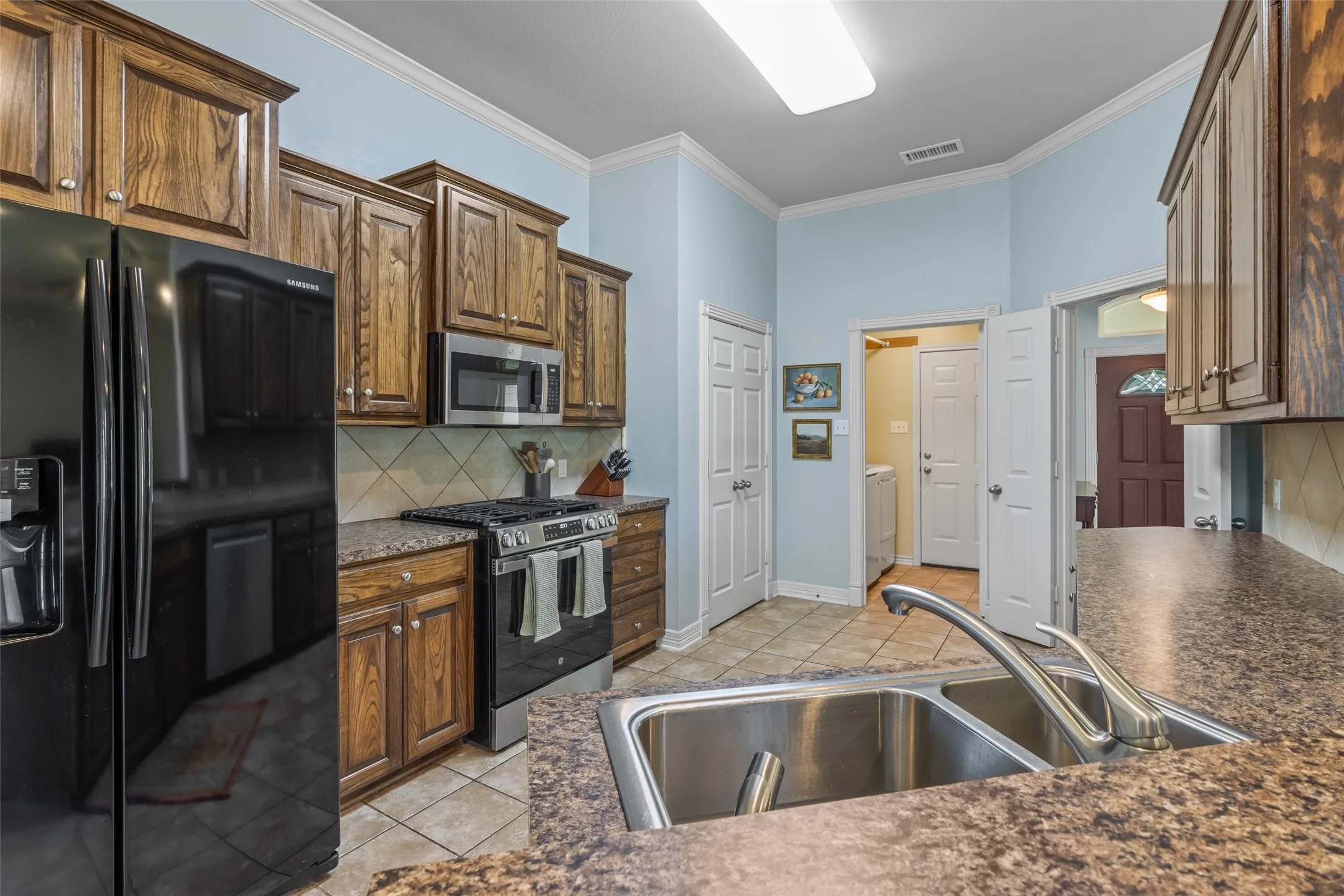 Kitchen featuring wood cabinetry, stainless steel appliances, a double basin sink, and tile flooring