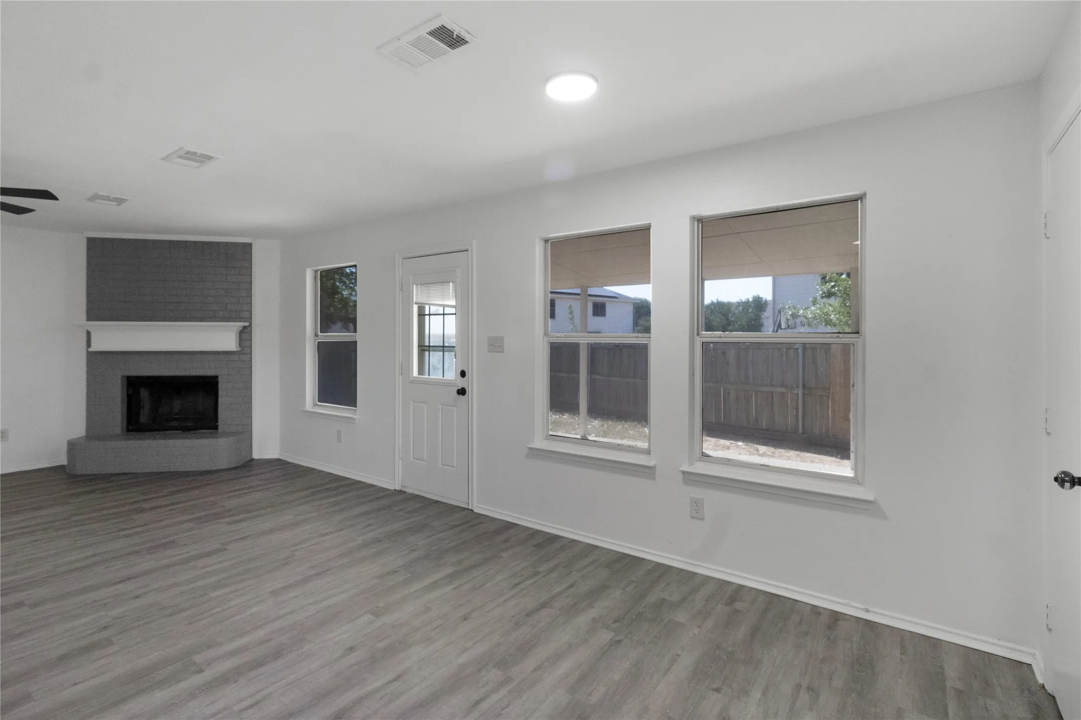 Gray brick fireplace with a white mantel, wood-finish flooring, recessed lighting, and multiple windows