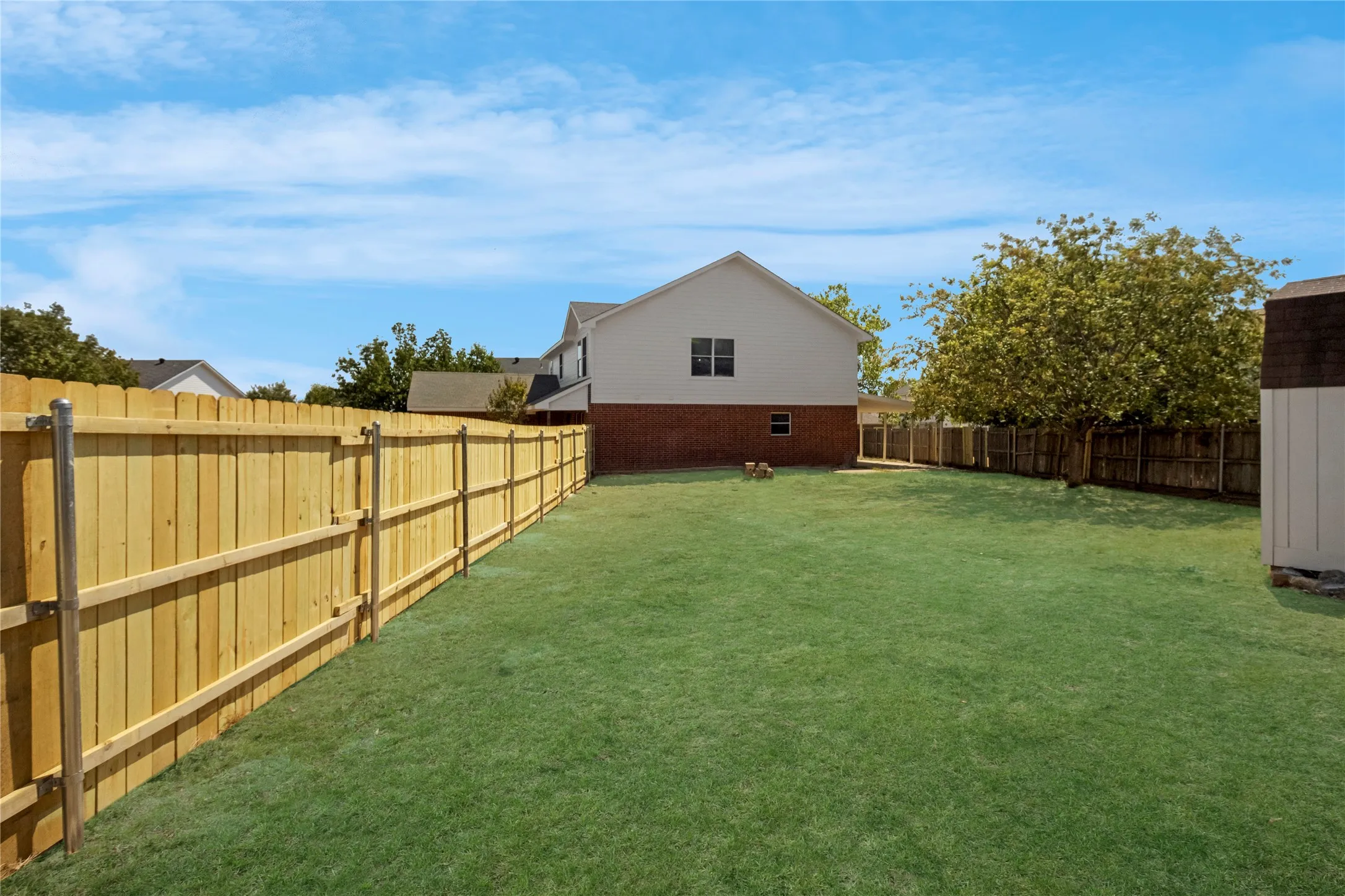 Expansive grassy yard with wood privacy fencing, a storage shed, and a two-story residence with brick and siding exterior