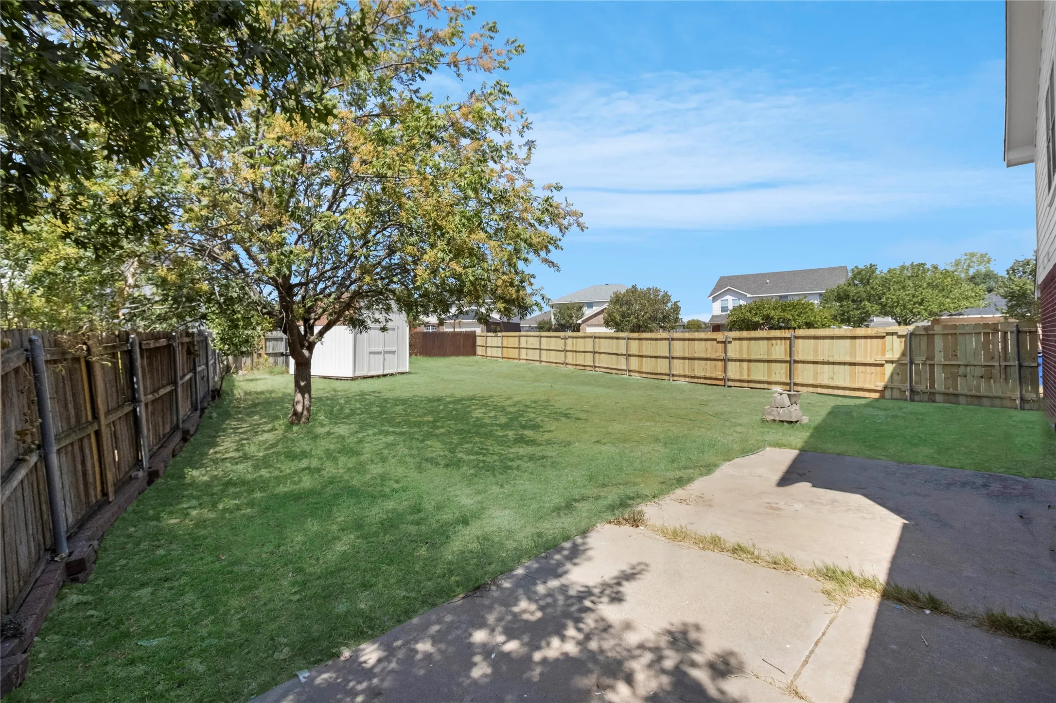 Expansive backyard featuring a manicured lawn, established tree, and a concrete patio