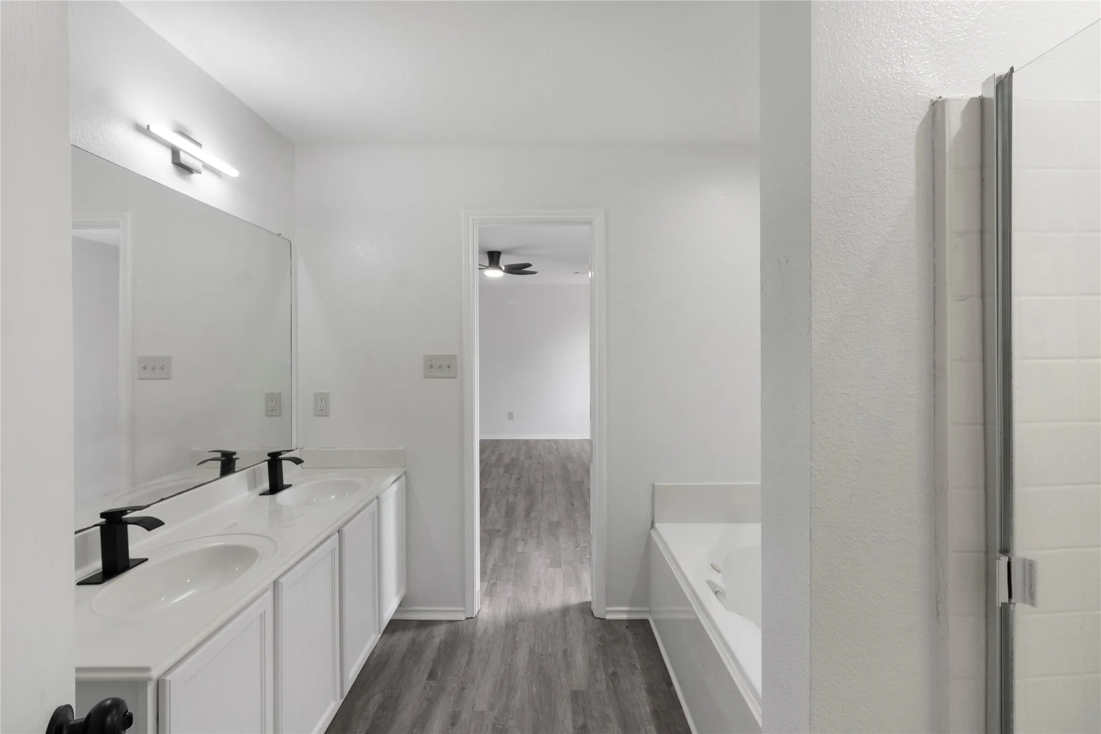 Spa-inspired primary bathroom featuring a dual-sink vanity with white cabinetry, black matte fixtures, and a quartz countertop