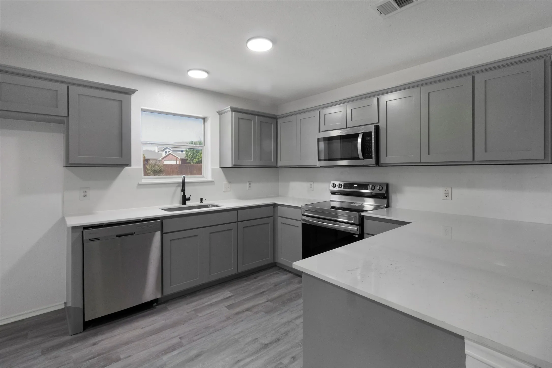 Kitchen featuring gray shaker-style cabinetry, stainless steel appliances, white countertops, a stainless steel sink with a black gooseneck faucet, and wood-finish flooring