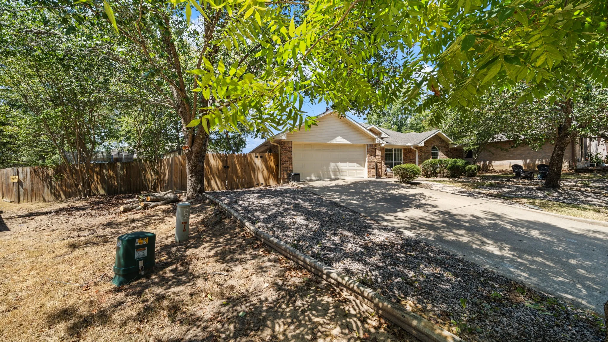 Brick exterior with an attached garage, paved driveway, and mature trees