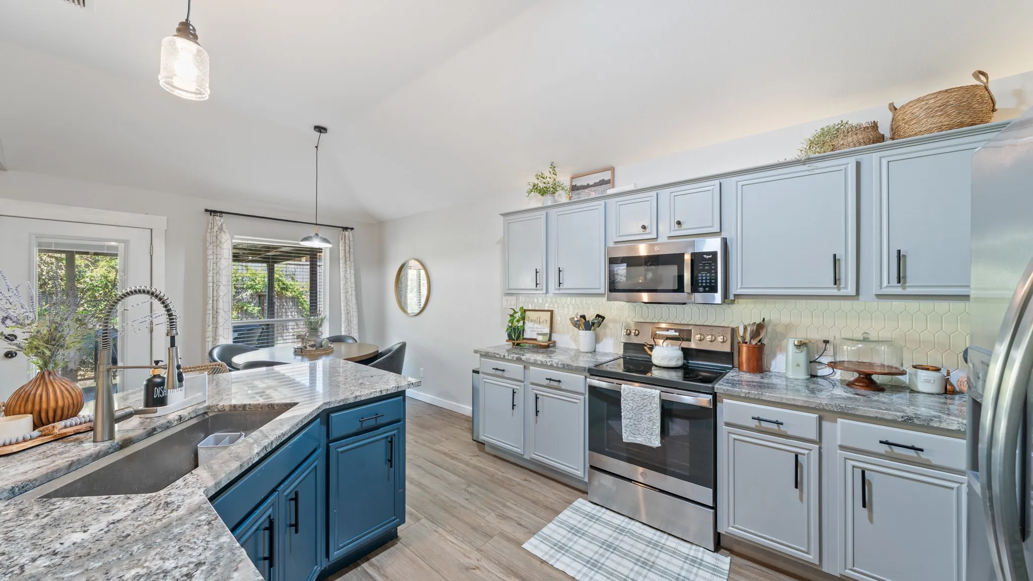 Kitchen featuring wood-finish flooring, light grey upper cabinetry, blue lower cabinetry, stainless steel appliances, and a hexagonal tile backsplash