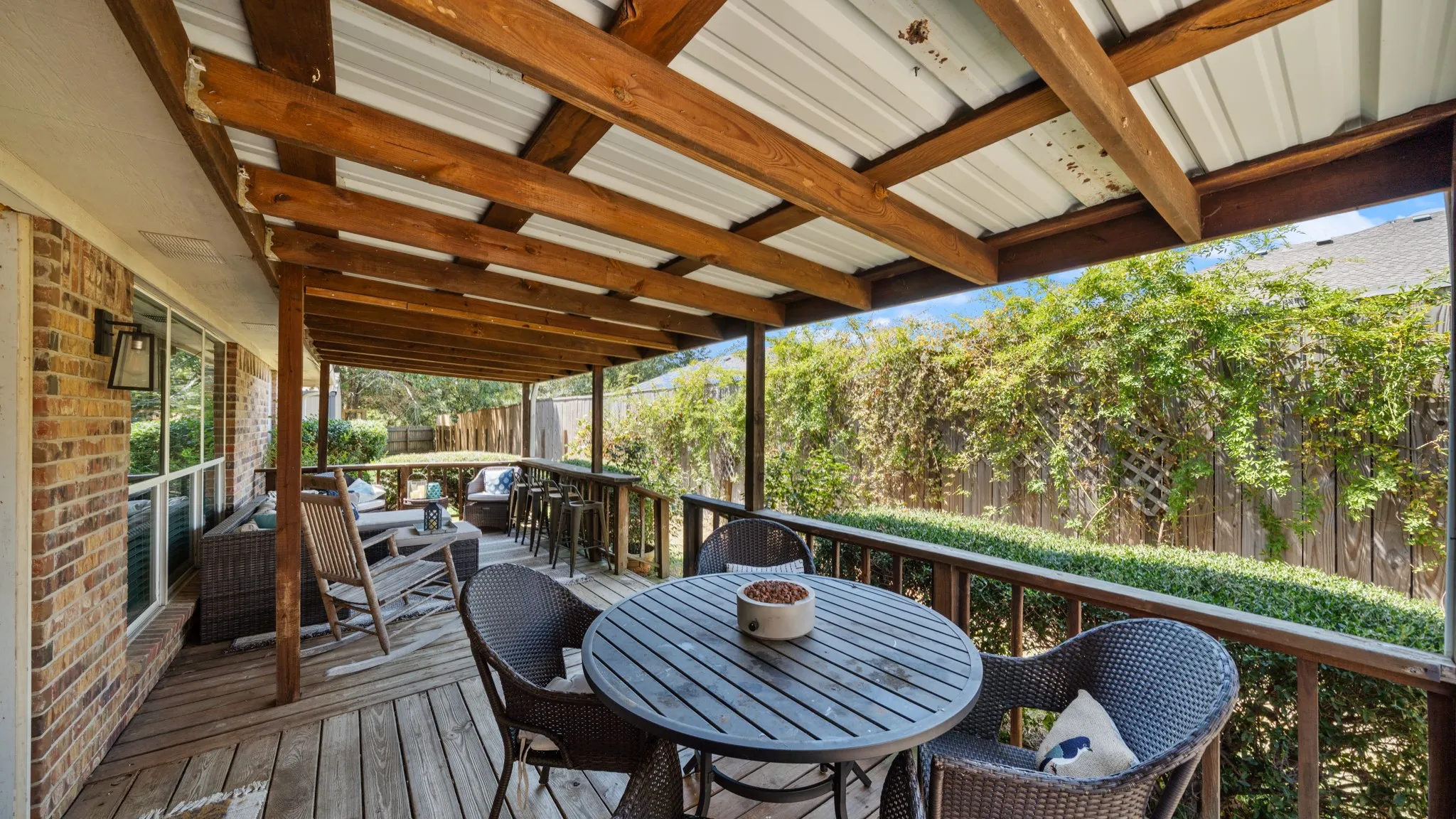 Expansive covered deck featuring a wood railing, brick exterior, and attached exterior lighting