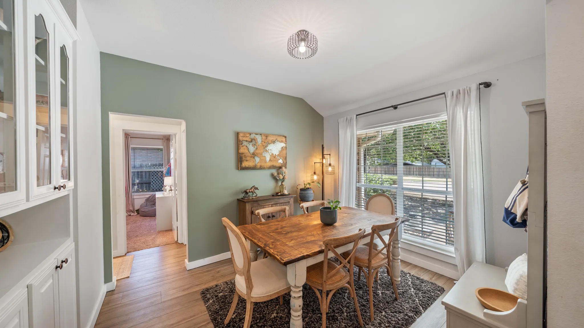 Built-in white cabinetry with glass-front doors, wood-finish flooring, a contemporary ceiling light fixture, and a large window with blinds