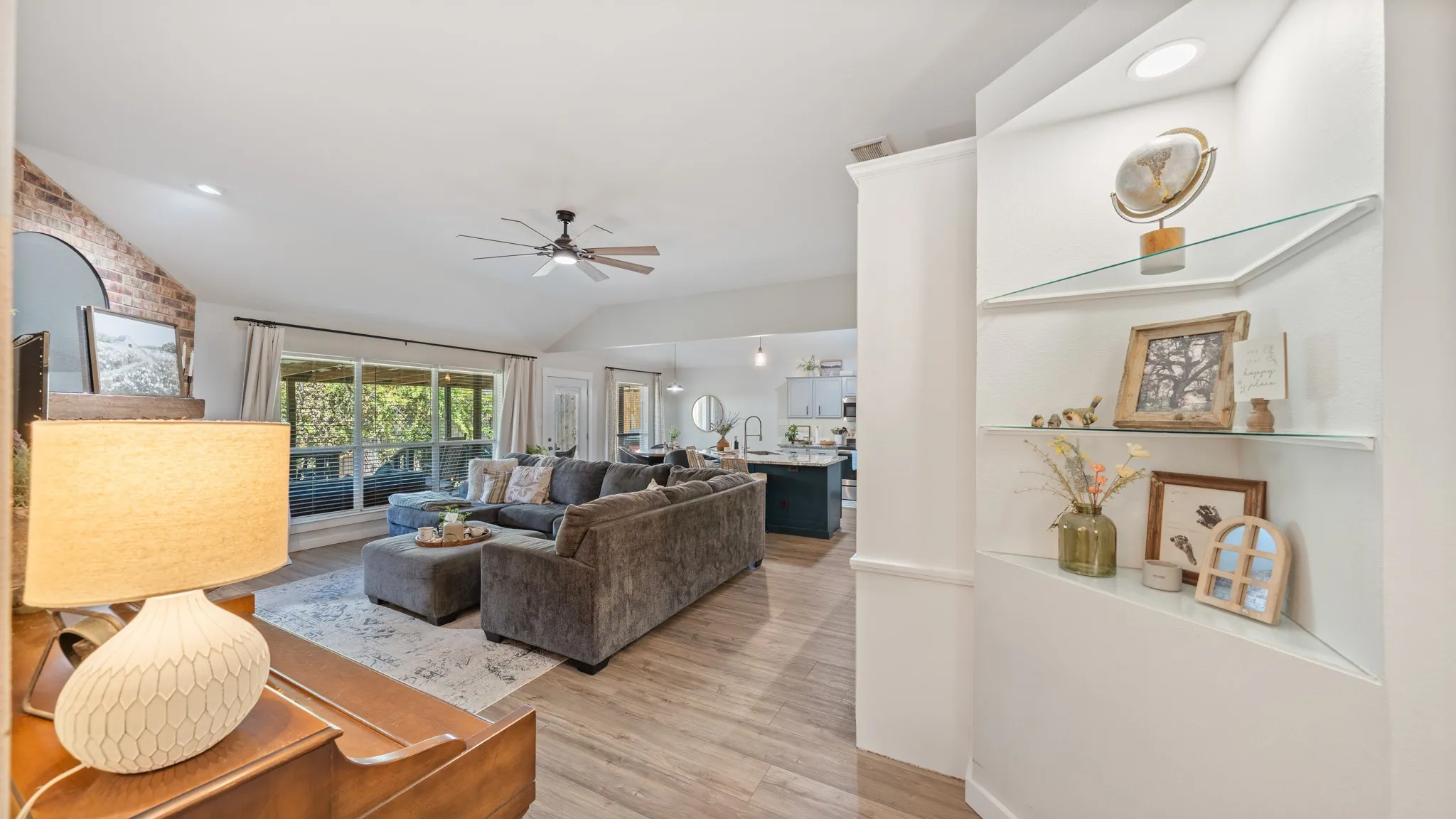 Integrated built-in shelving with glass shelves, vaulted ceiling, wood-finish flooring, and a ceiling fan
