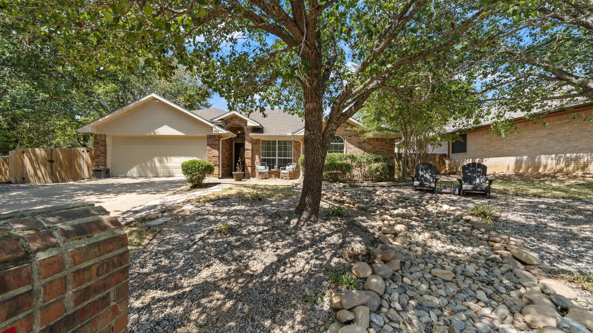 Brick exterior, attached two-car garage, mature front yard trees, and a stone-lined dry creek bed