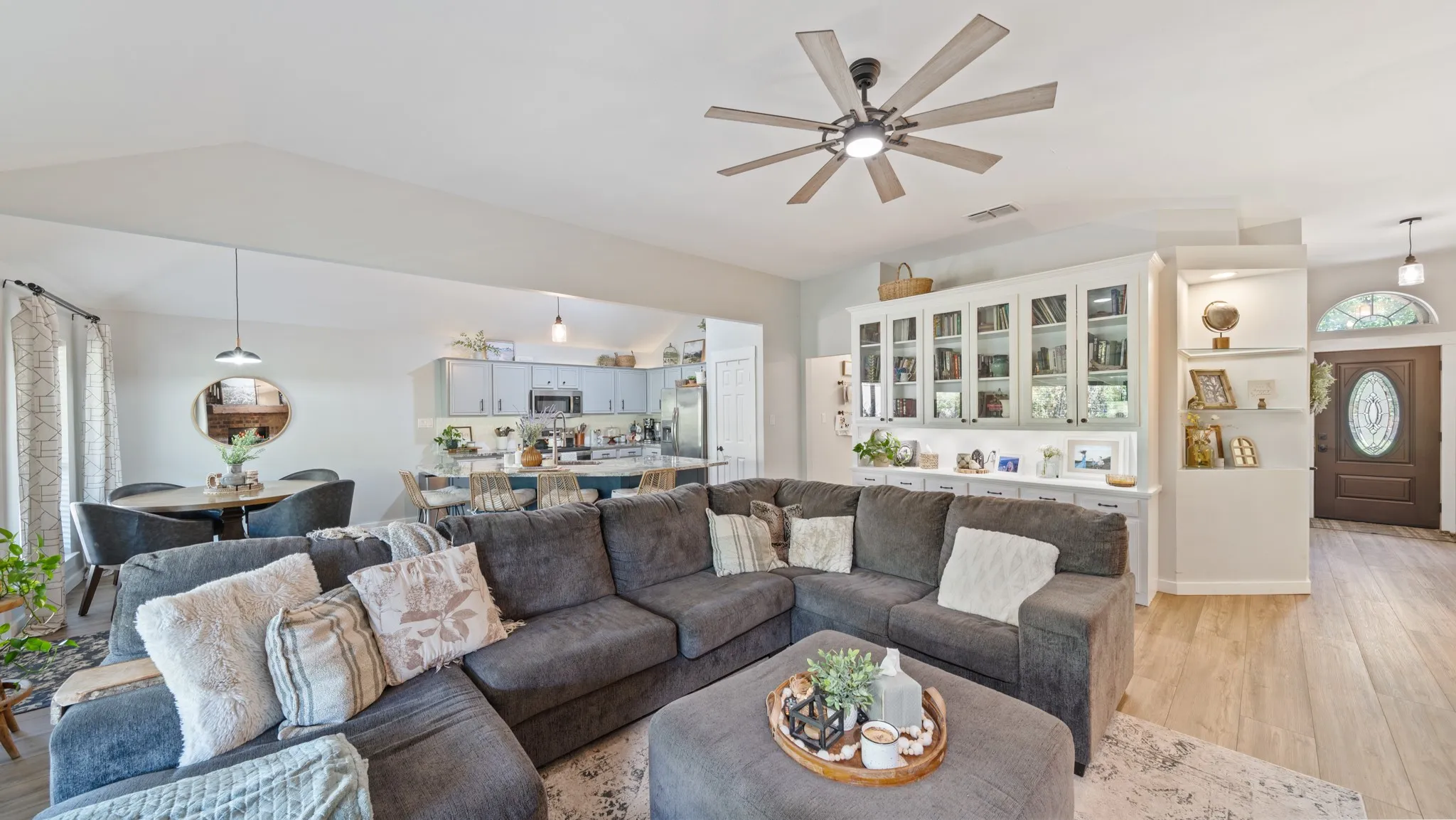 Open-concept living area featuring wood-finish flooring, a contemporary ceiling fan, and built-in cabinetry with glass-front uppers