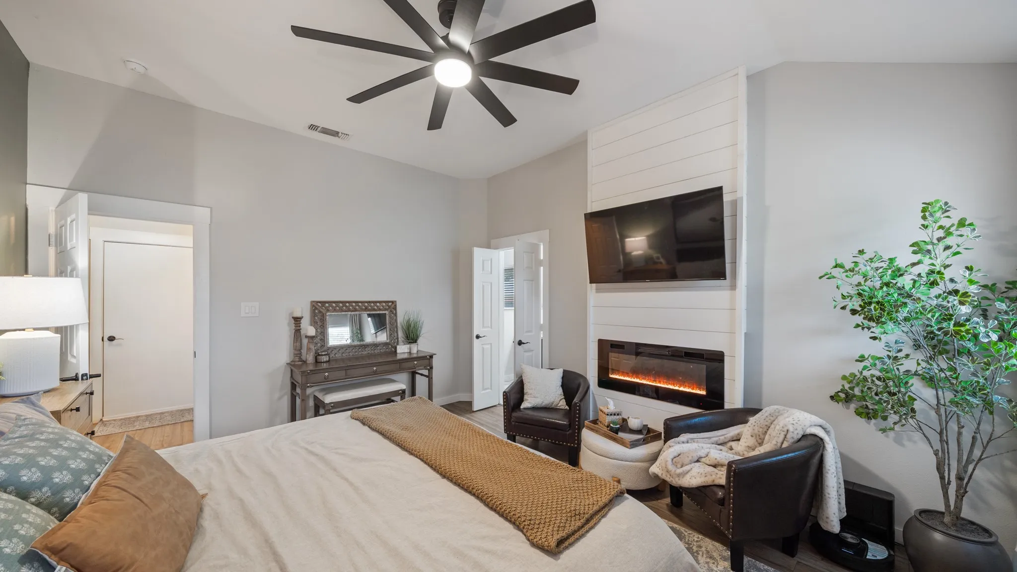 Vaulted ceiling with a ceiling fan, accent wall with a built-in electric fireplace, and dark wood-finish flooring