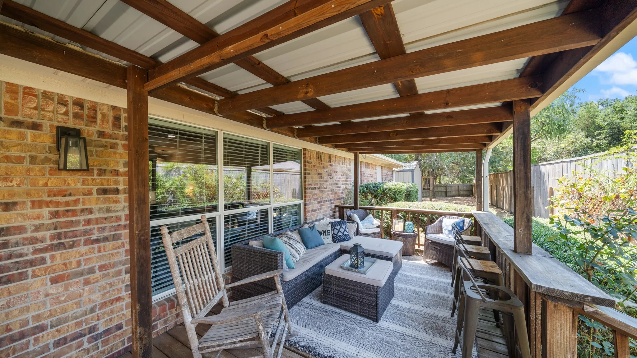 Covered patio featuring a wood-beam ceiling, brick exterior wall, multiple windows, and a wood railing with a built-in counter