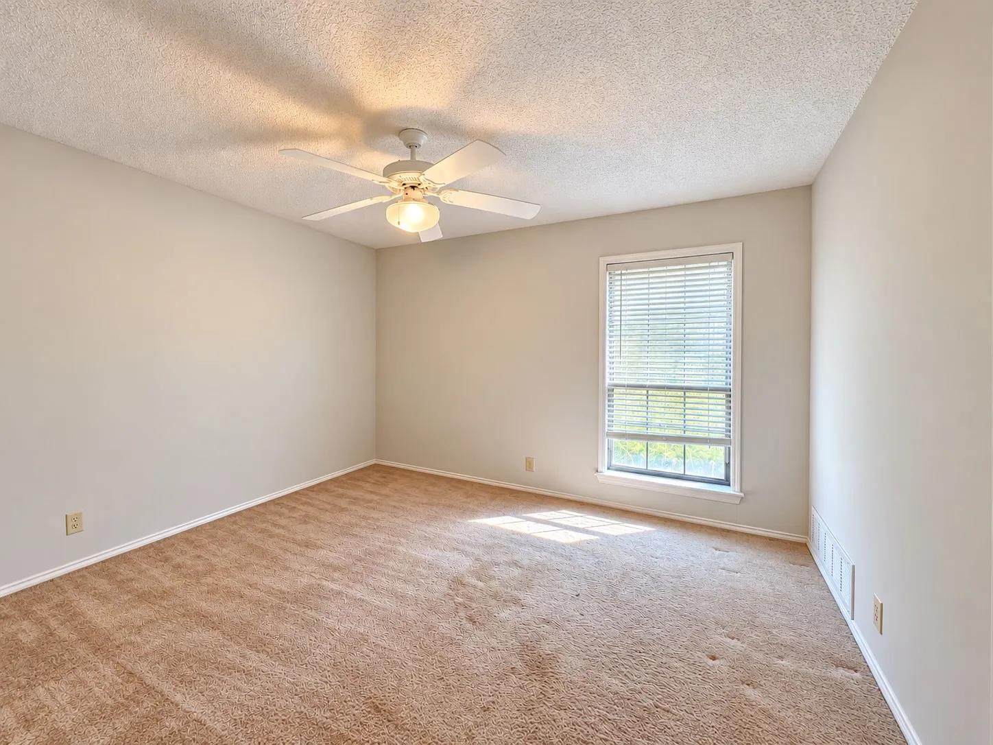Neutral-toned walls, textured ceiling, brown carpeting, window with blinds, and a ceiling fan with integrated lighting