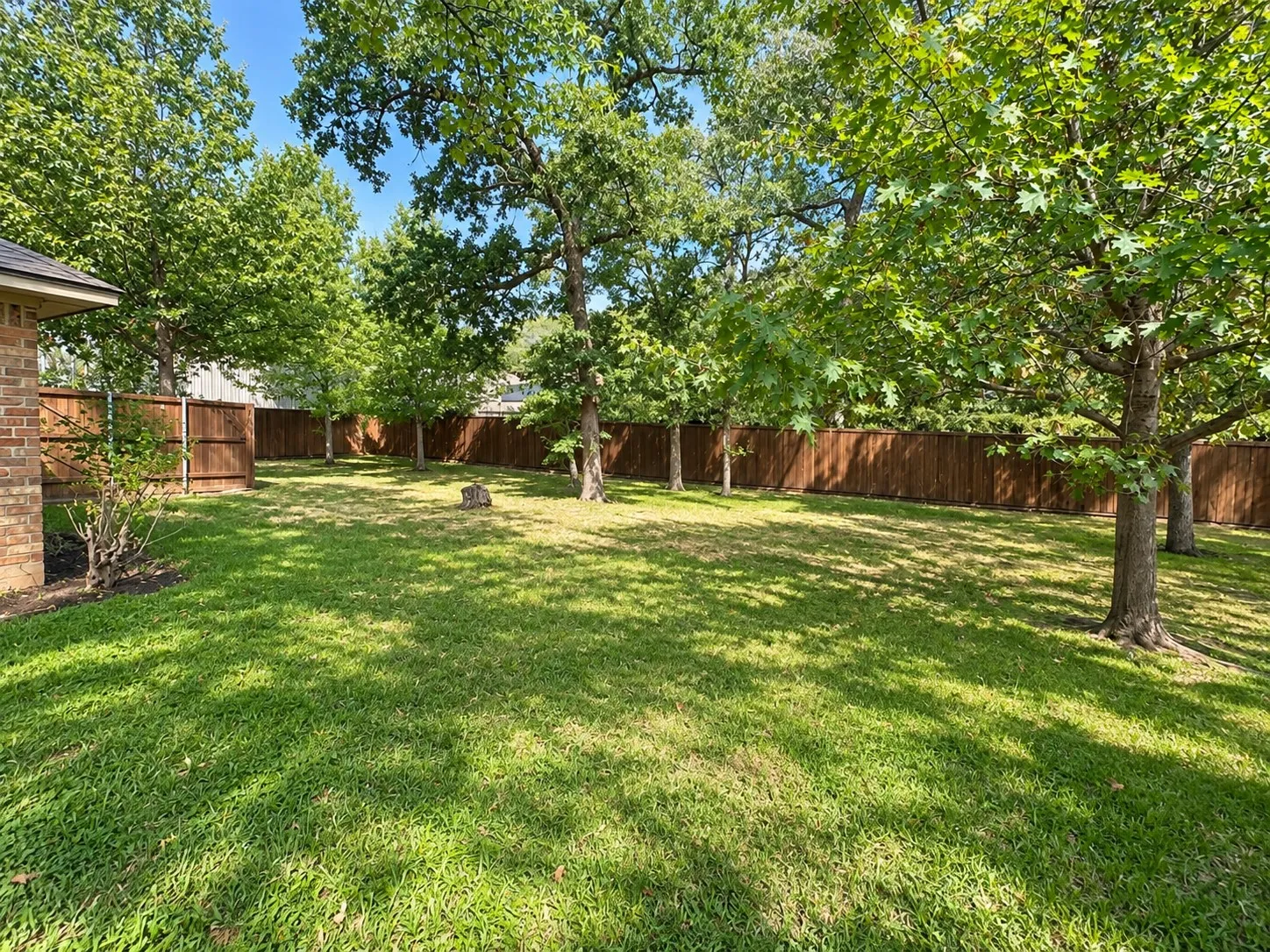 Expansive lawn featuring mature trees, a privacy fence, and brick exterior detailing