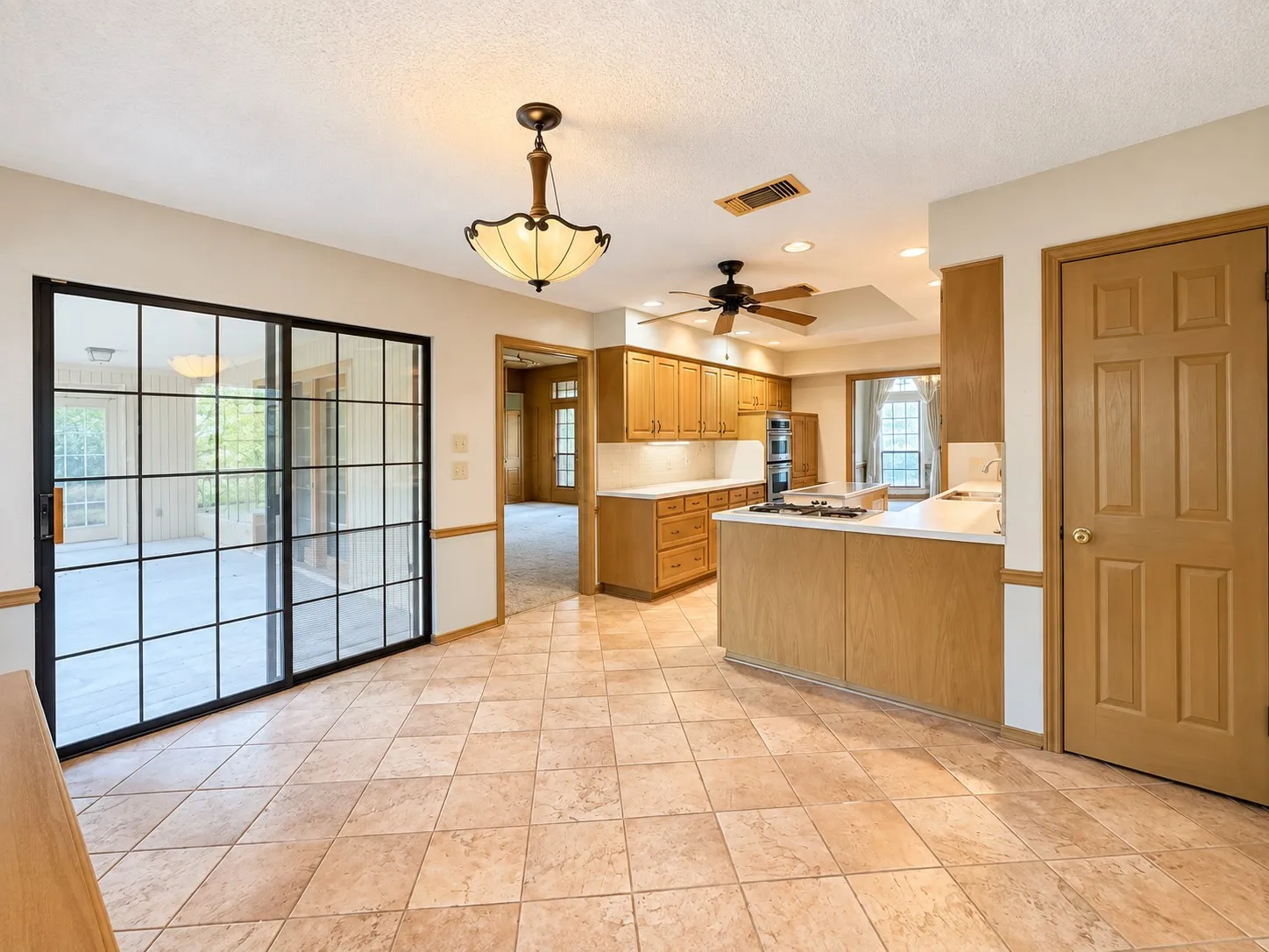 Tile flooring, wood cabinetry, white countertops, built-in ovens, and a ceiling fan