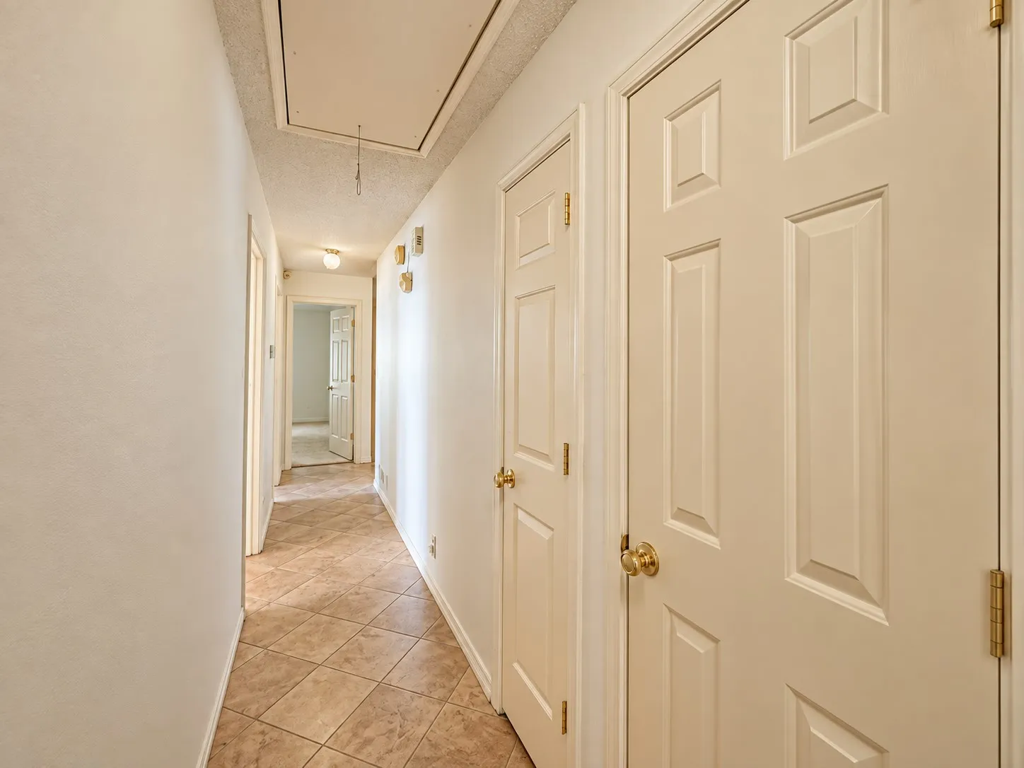 Hallway featuring neutral-toned walls, tile flooring, and panel doors with brass hardware