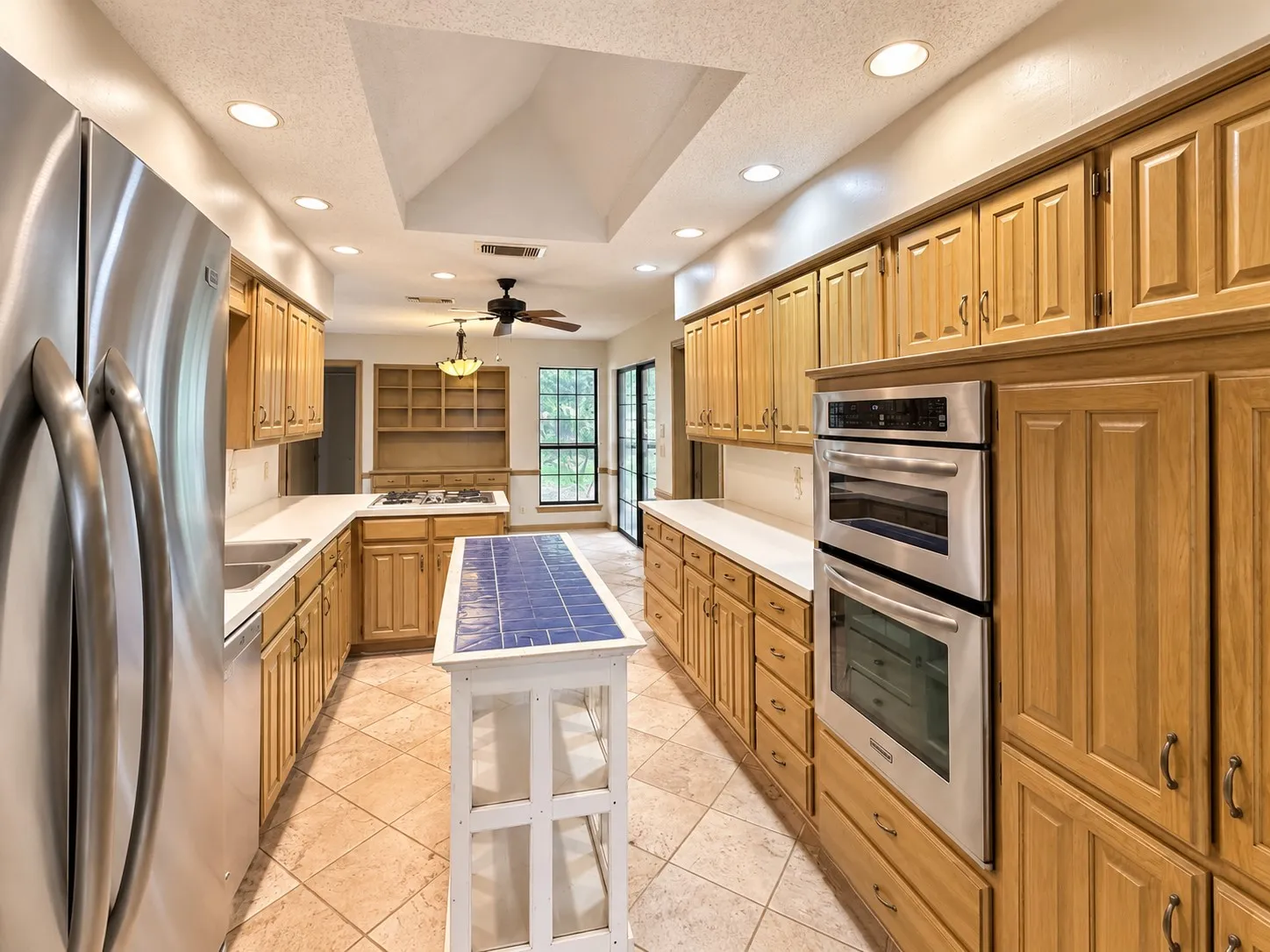 Galley kitchen featuring abundant wood cabinetry, stainless steel double ovens, recessed lighting, a central skylight, and tile flooring