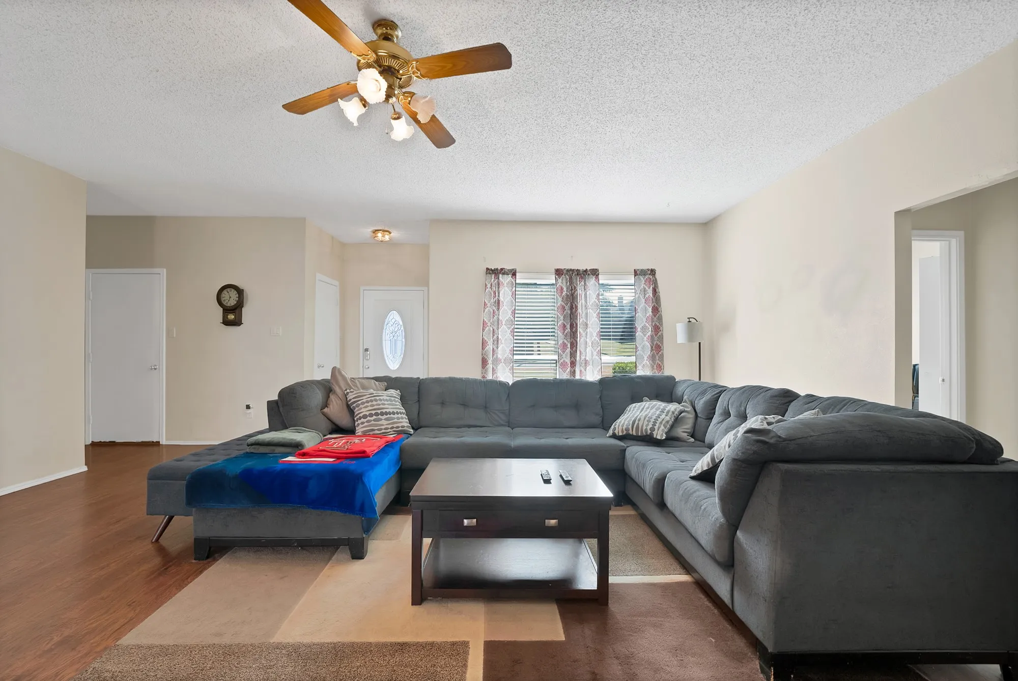 Spacious living area featuring wood-finish flooring, a ceiling fan with integrated lighting, and multiple windows