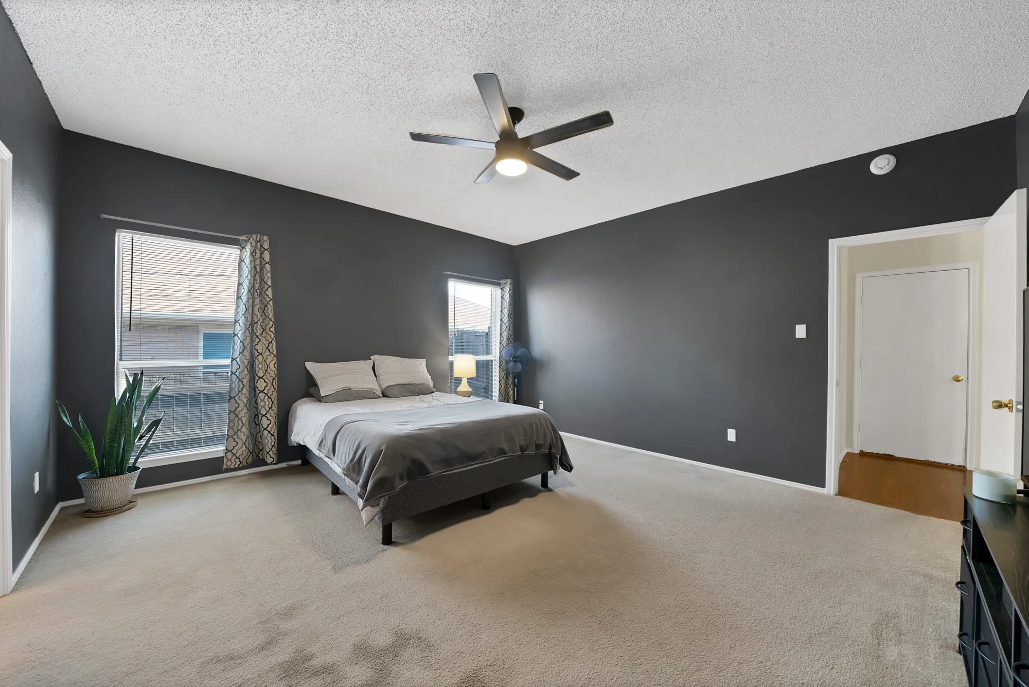 Vaulted ceiling with a ceiling fan, dual windows, dark wall paint, and light-toned carpeting