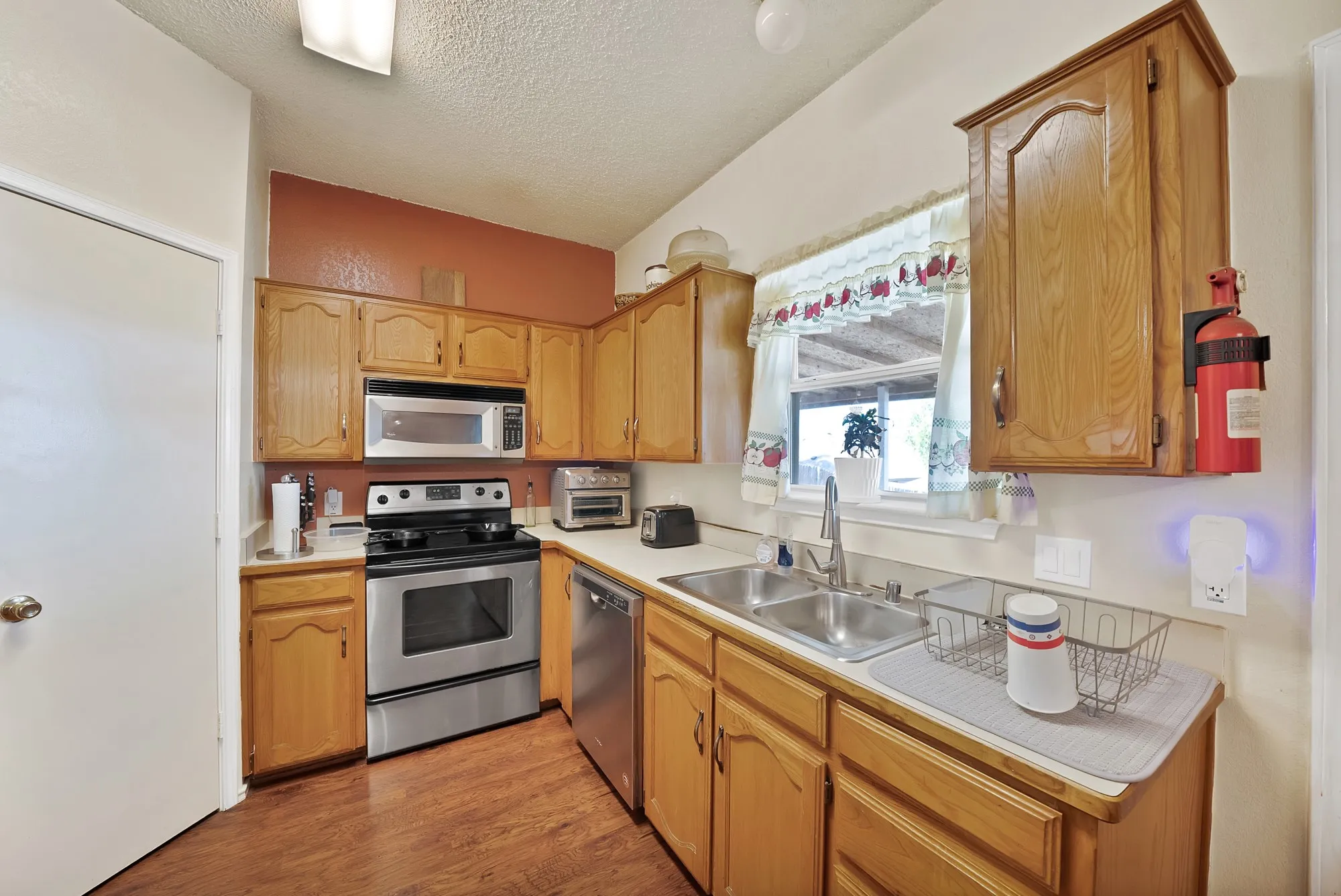 Kitchen with wood-finish flooring, stainless steel appliances, wood cabinetry, and a double basin sink