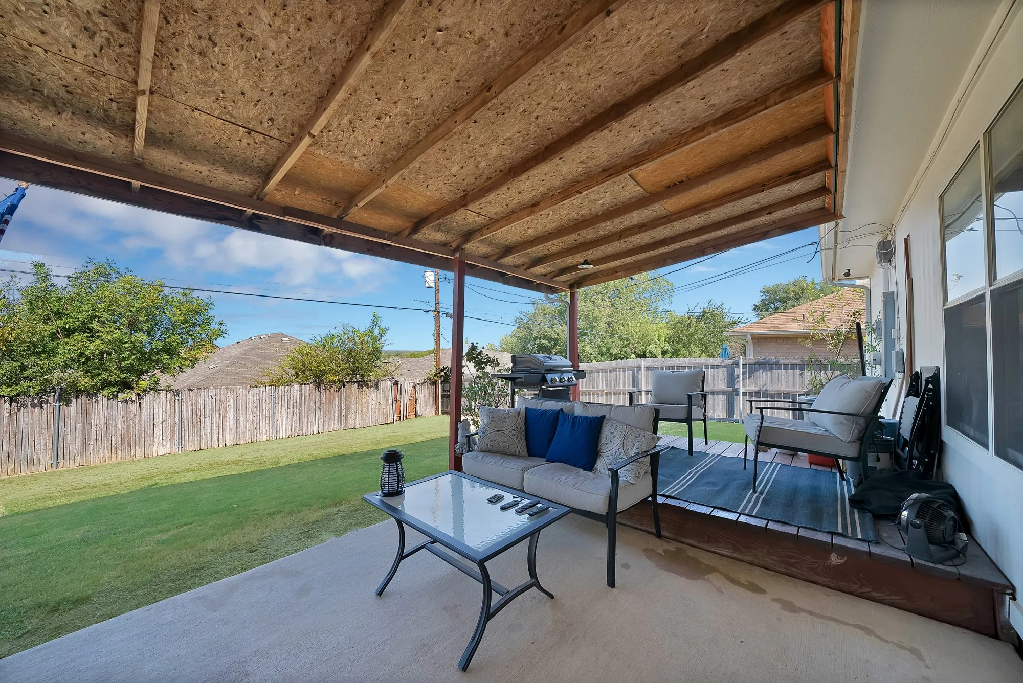 Covered concrete patio with a wood-framed roof, a raised wood deck, and a fenced backyard with a manicured lawn