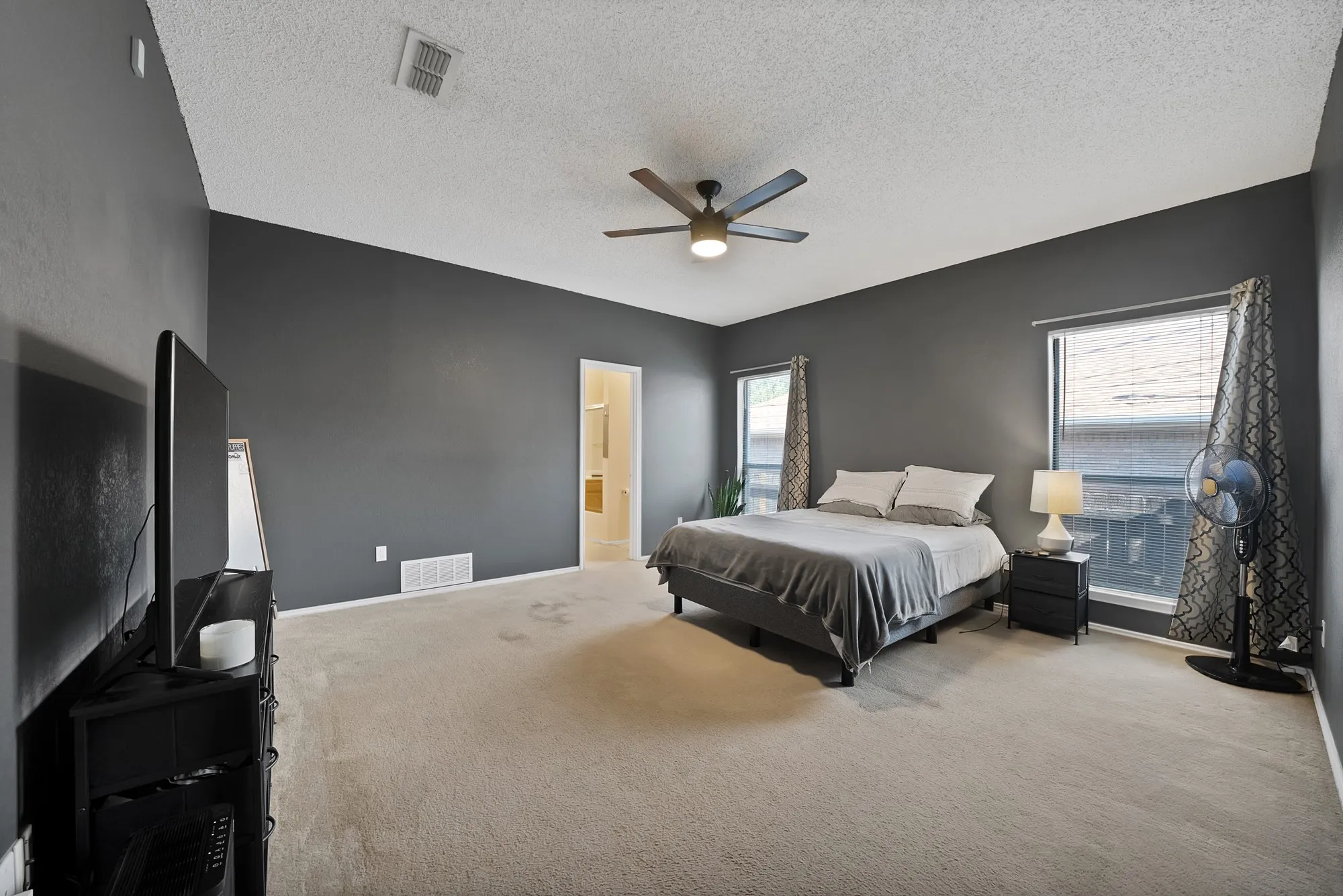 Spacious room featuring vaulted ceilings, neutral carpeting, dual windows, and a ceiling fan with integrated lighting