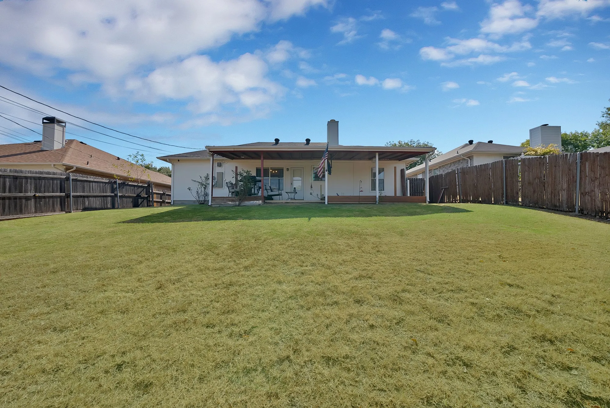 Expansive backyard featuring a covered patio, wood deck, and perimeter fencing