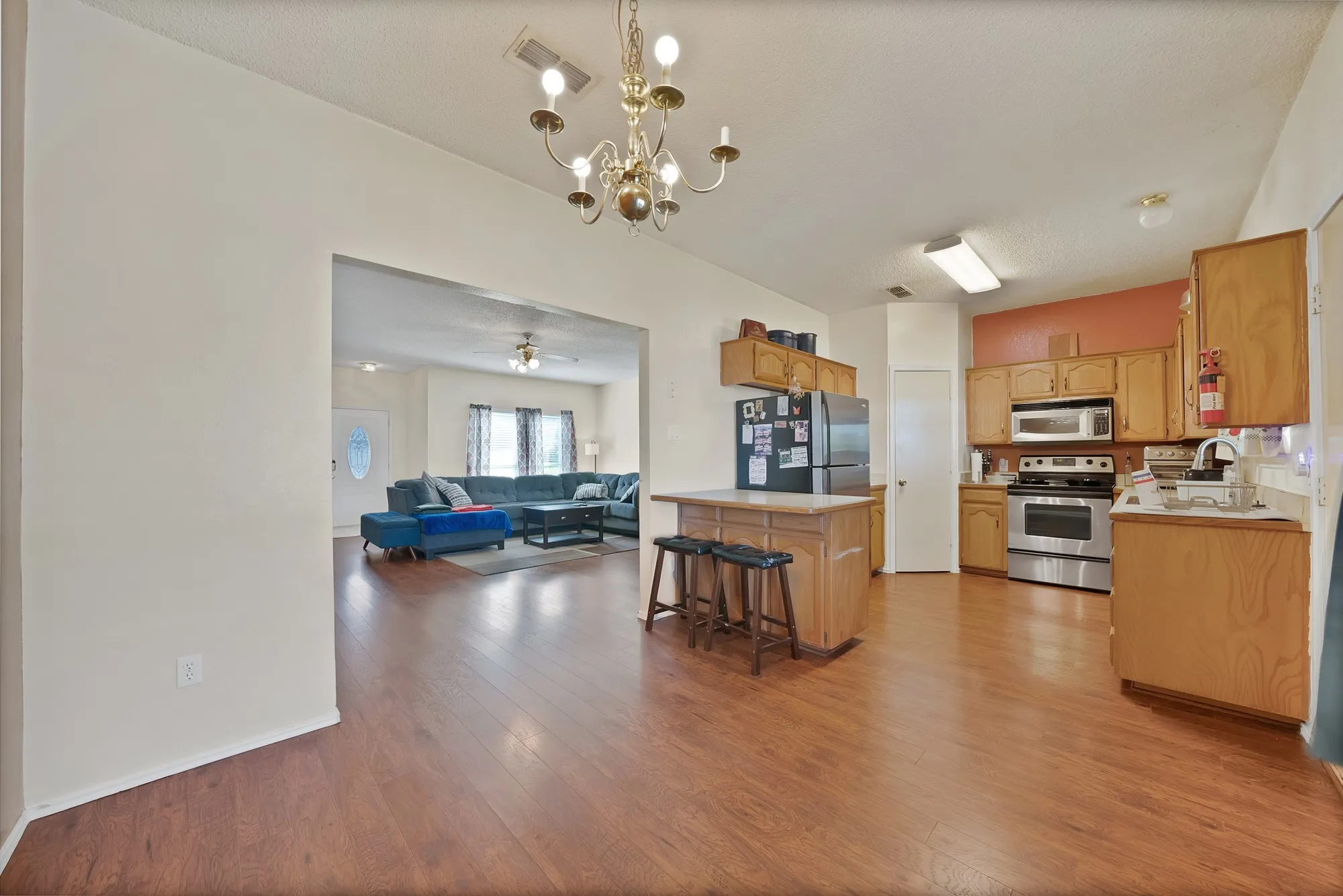 Hardwood-finish flooring throughout, kitchen island with seating, stainless steel appliances, and a decorative chandelier