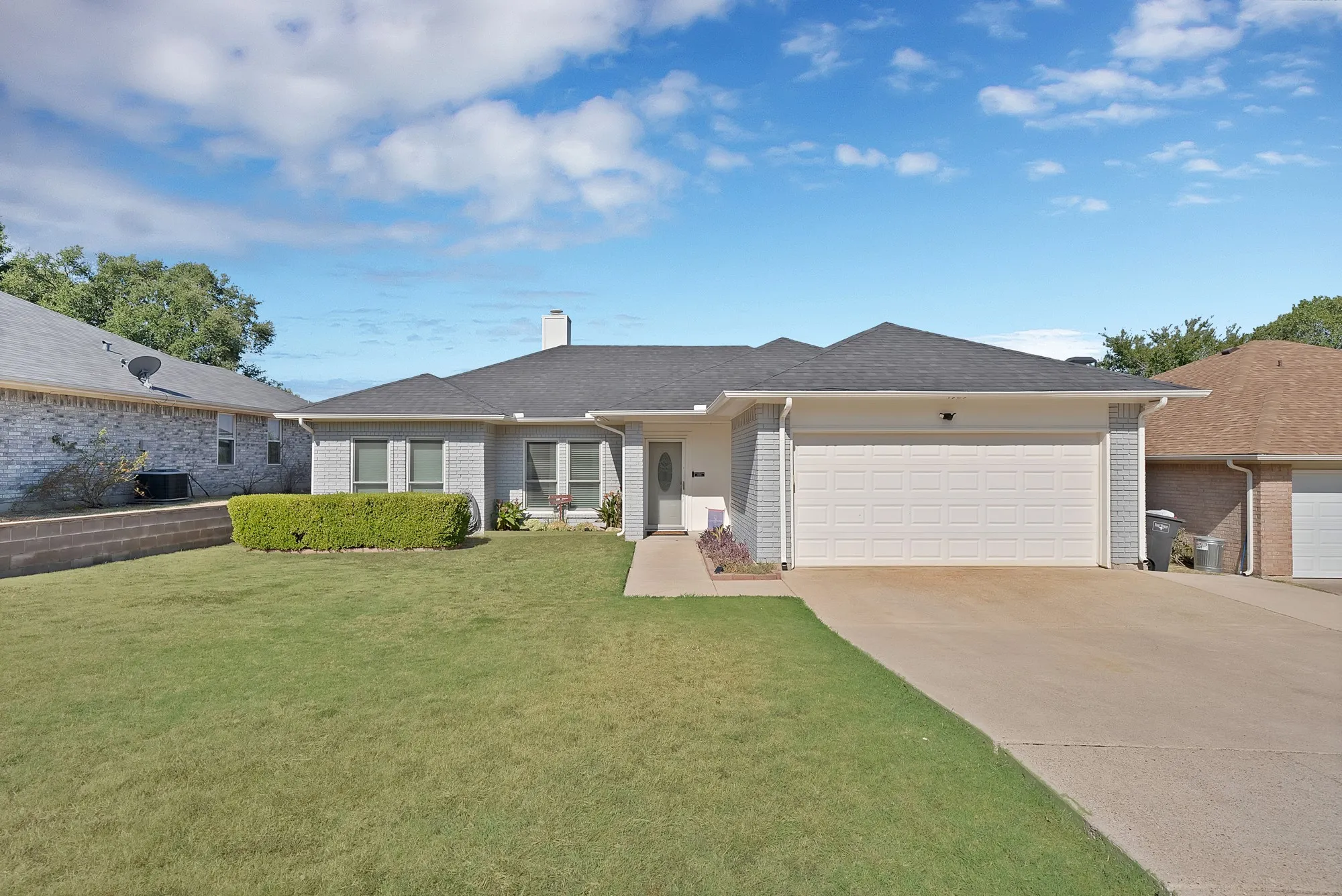 Ranch-style residence featuring a gray brick and siding exterior, a two-car garage, a dark shingle roof, and a concrete driveway