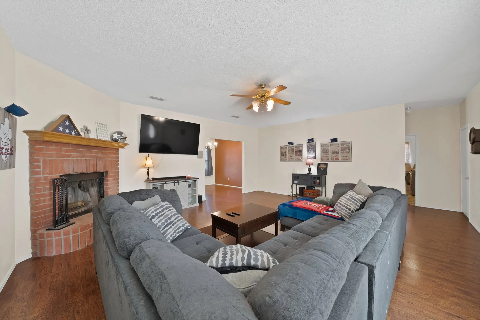 Spacious living area featuring a brick fireplace, wood-finish flooring, and a ceiling fan