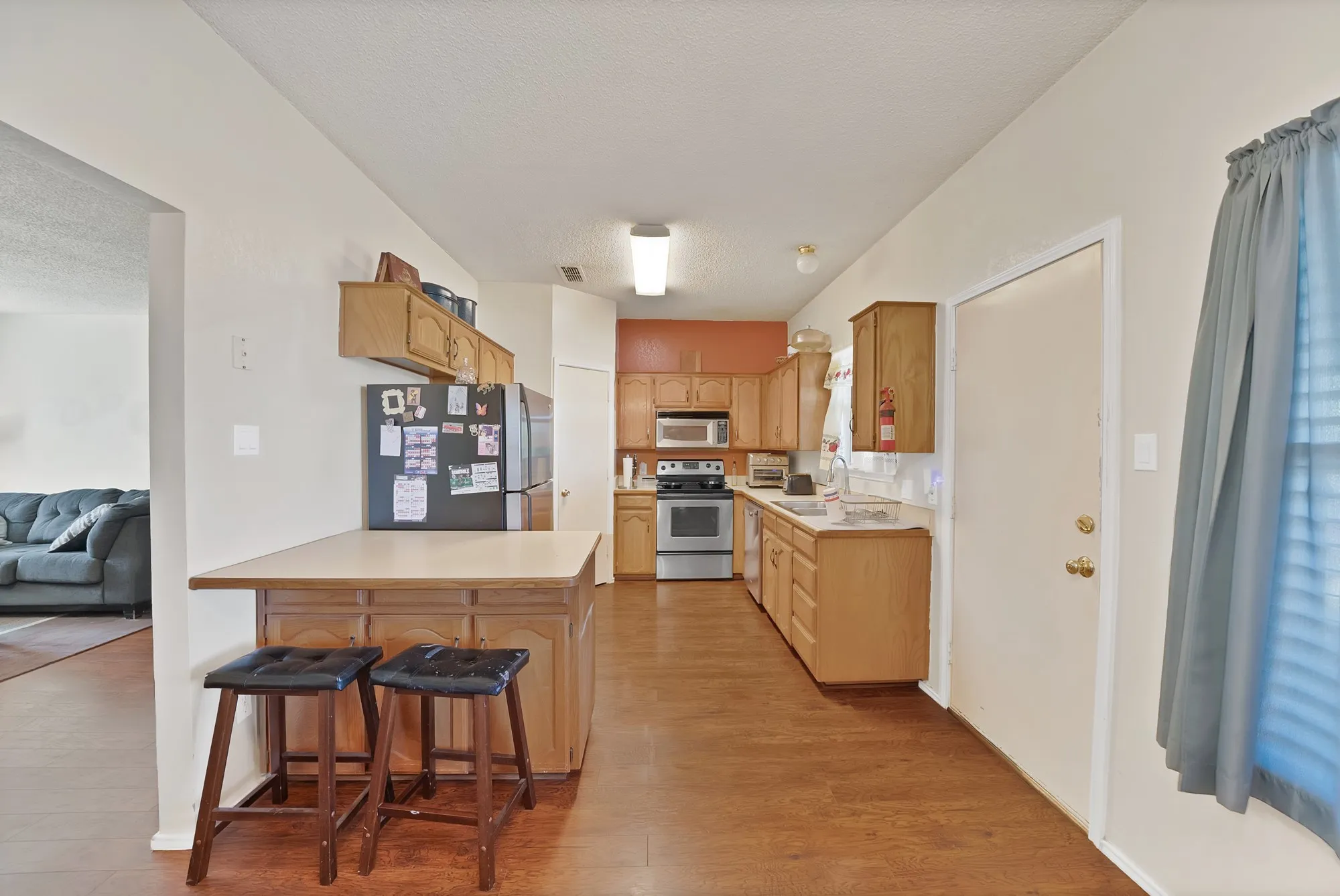 Wood-finish flooring throughout, wood cabinetry, stainless steel appliances, and a built-in breakfast bar