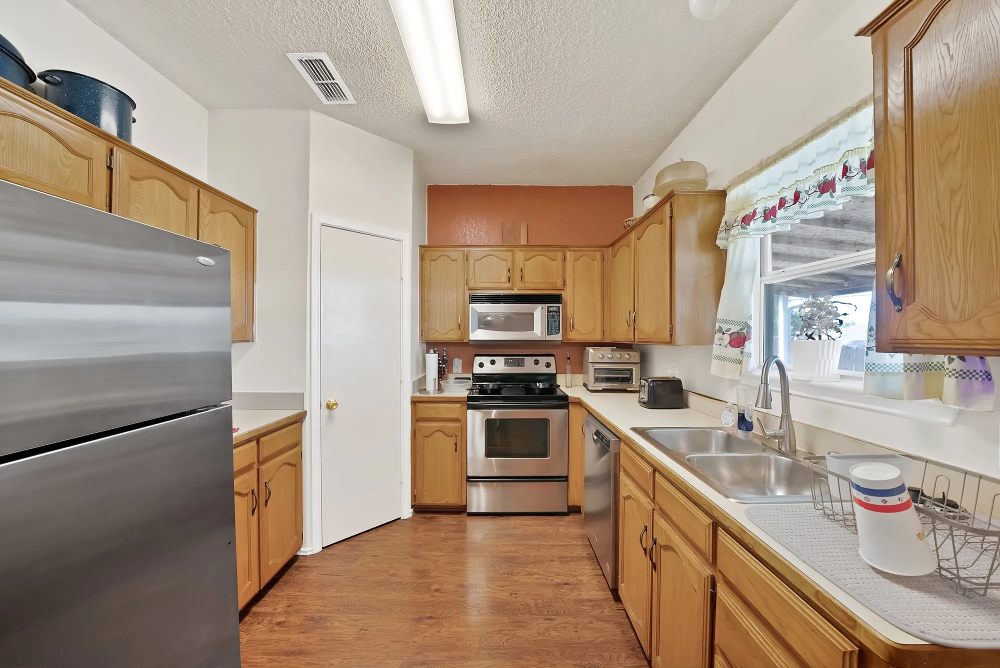 Kitchen featuring wood-finish flooring, light wood cabinetry, stainless steel appliances, and a double basin sink
