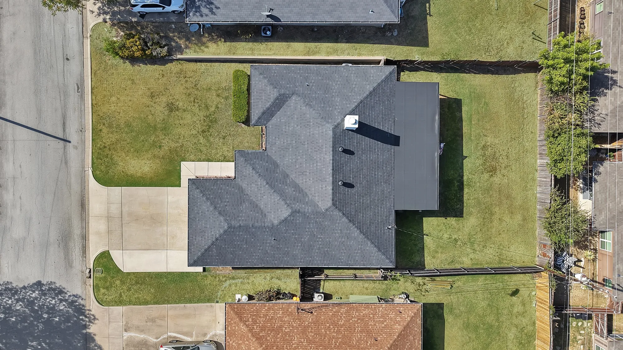 Asphalt shingle roofing with a chimney, expansive grassy yard, and paved driveway